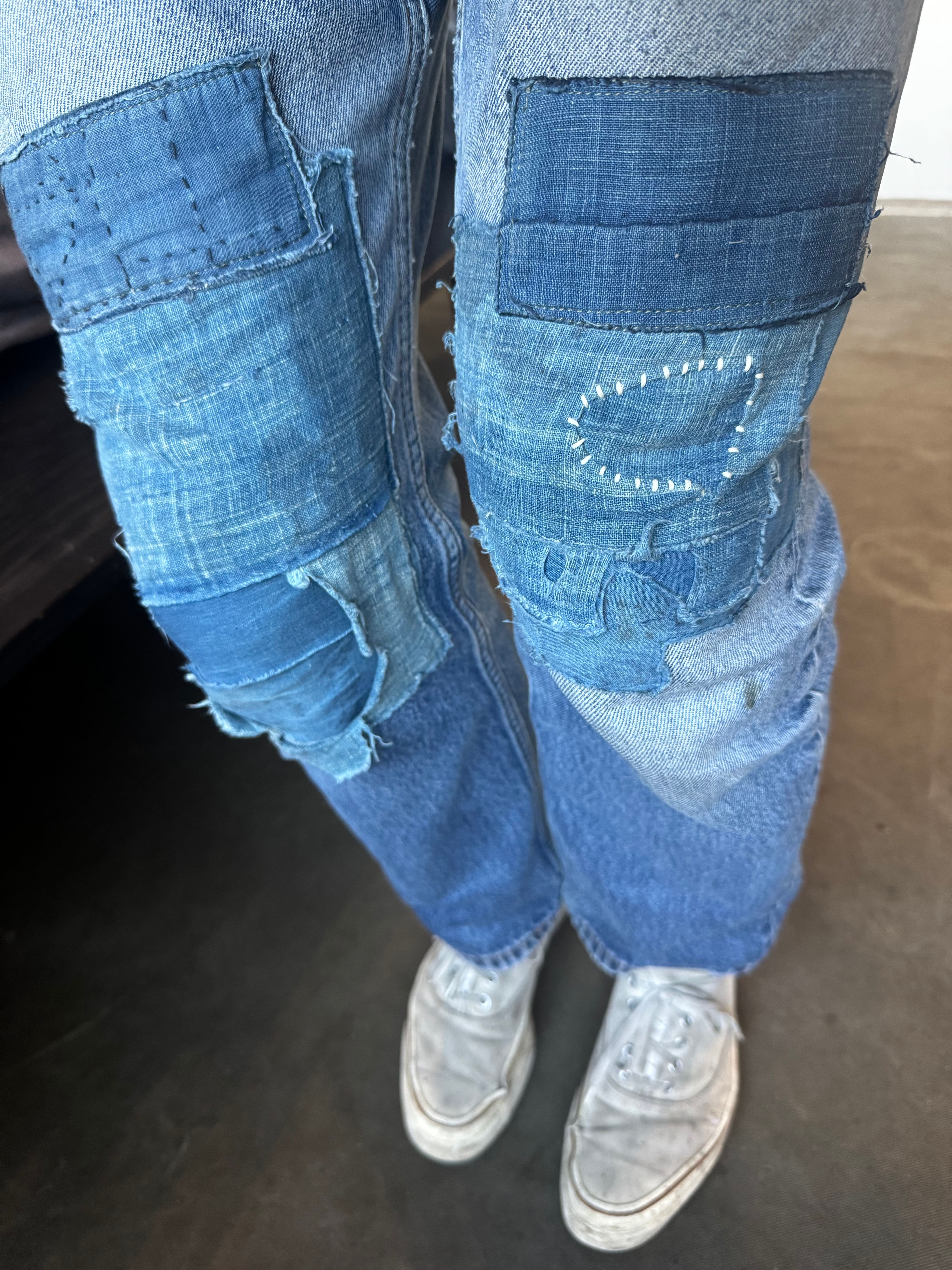 a person wearing blue jeans with patches on the knees and white sneakers .