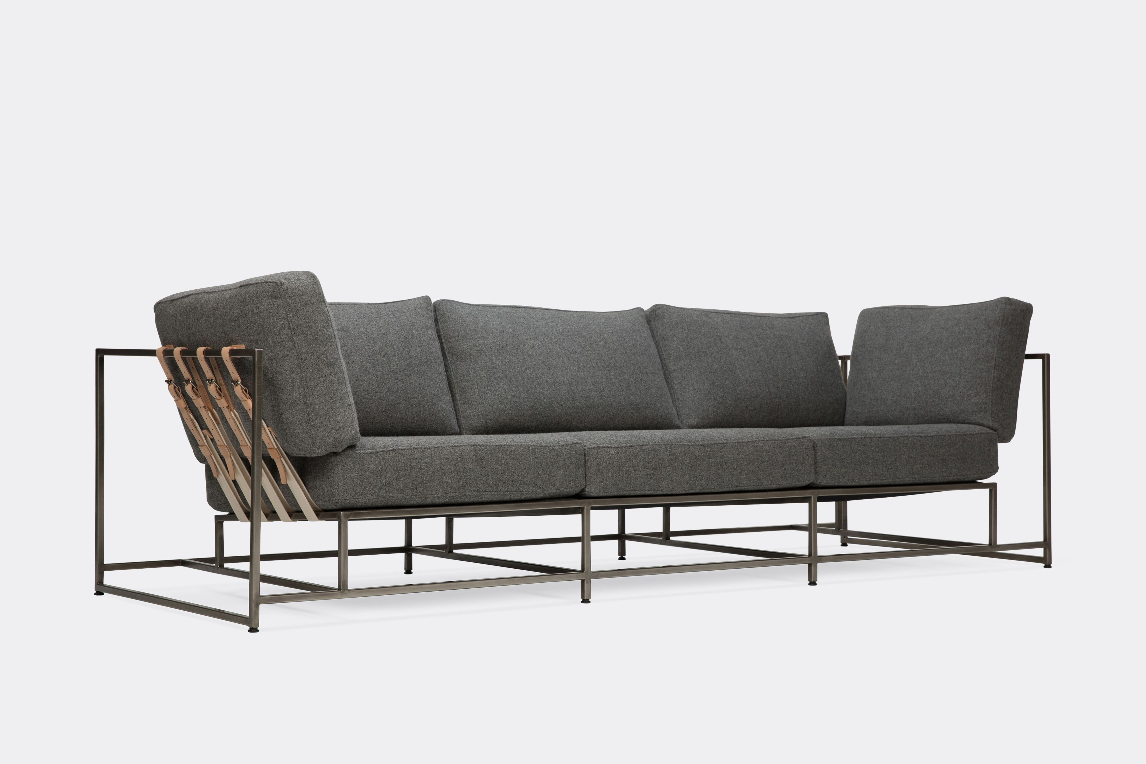 sideview of sofa with grey wool upholstery and veg tan leather belts on antique nickel metal frame