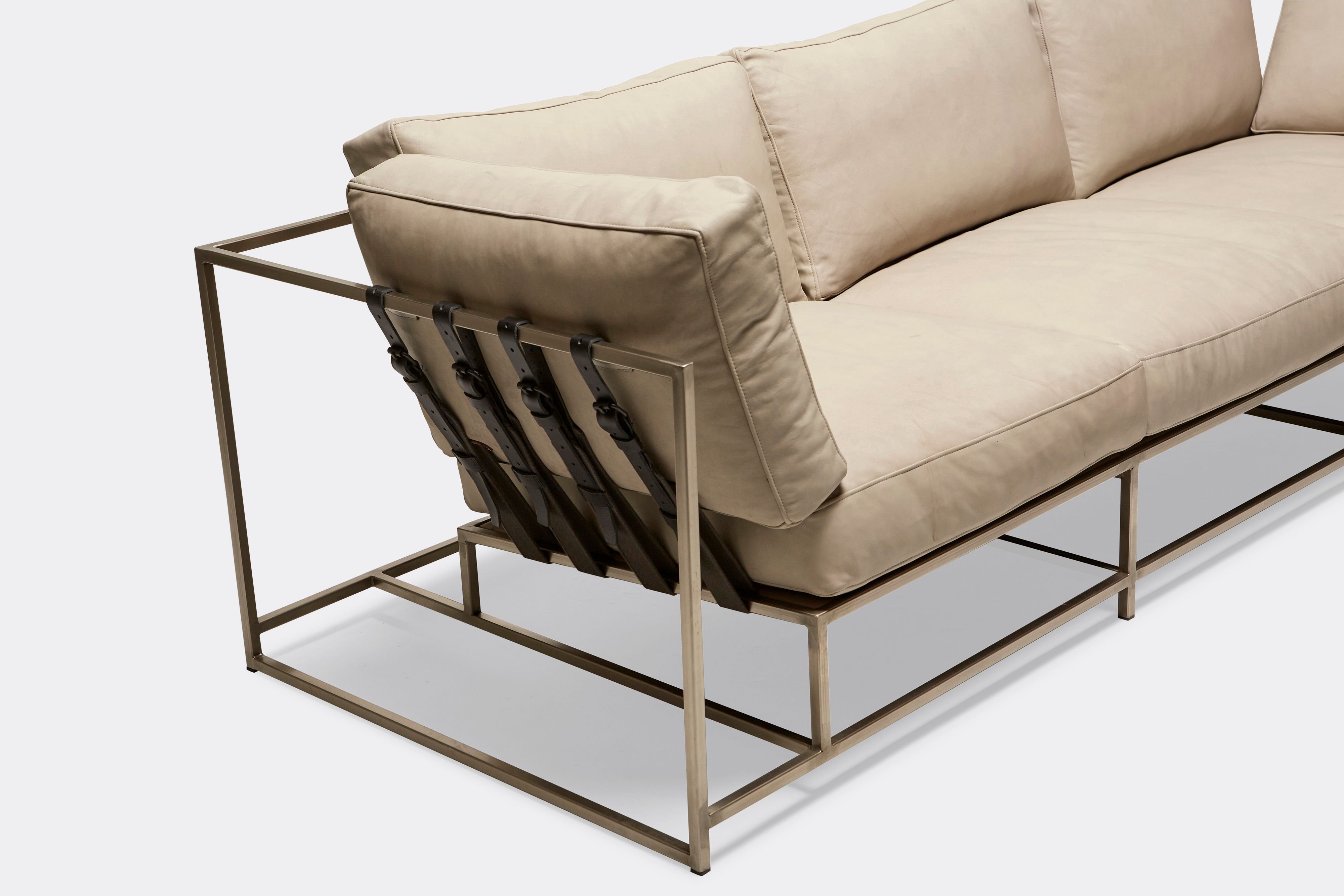 sideview of Sofa with cream leather upholstery and black leather belts on antique nickel metal frame