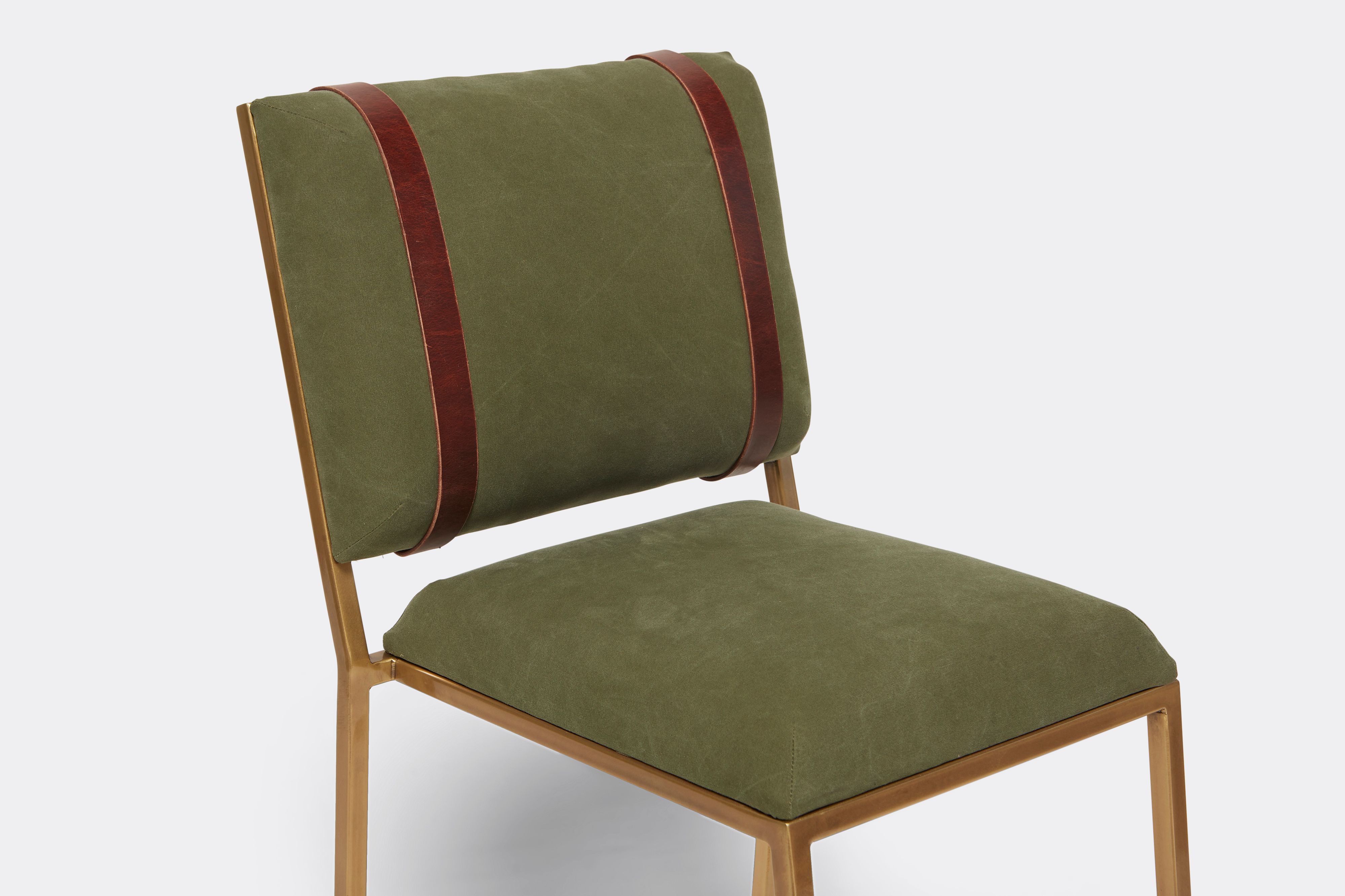 Detail of barstool with military canvas upholstery and brown leather belts on antique brass metal legs