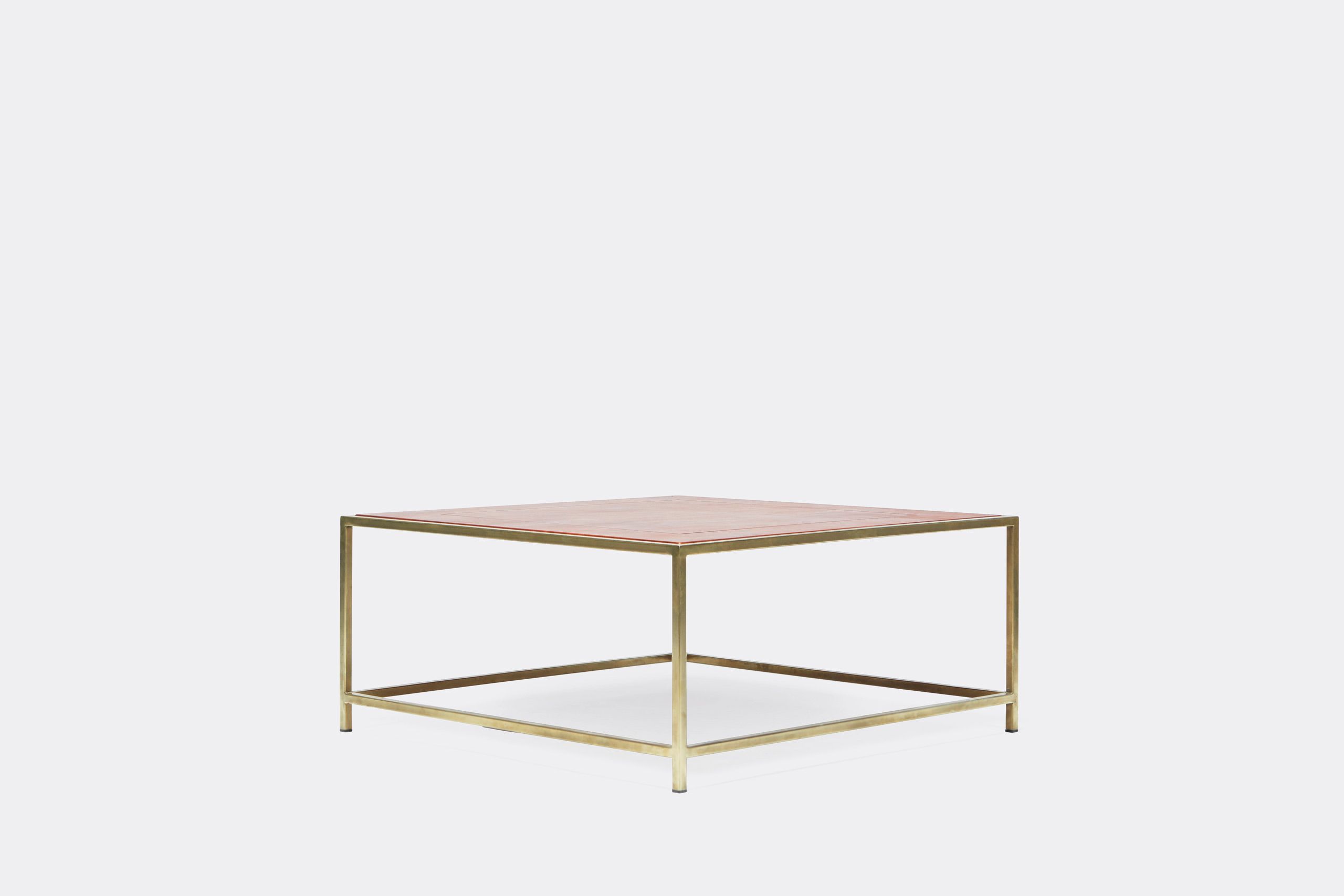 a square coffee table with a leather top and a brass frame on a white background .
