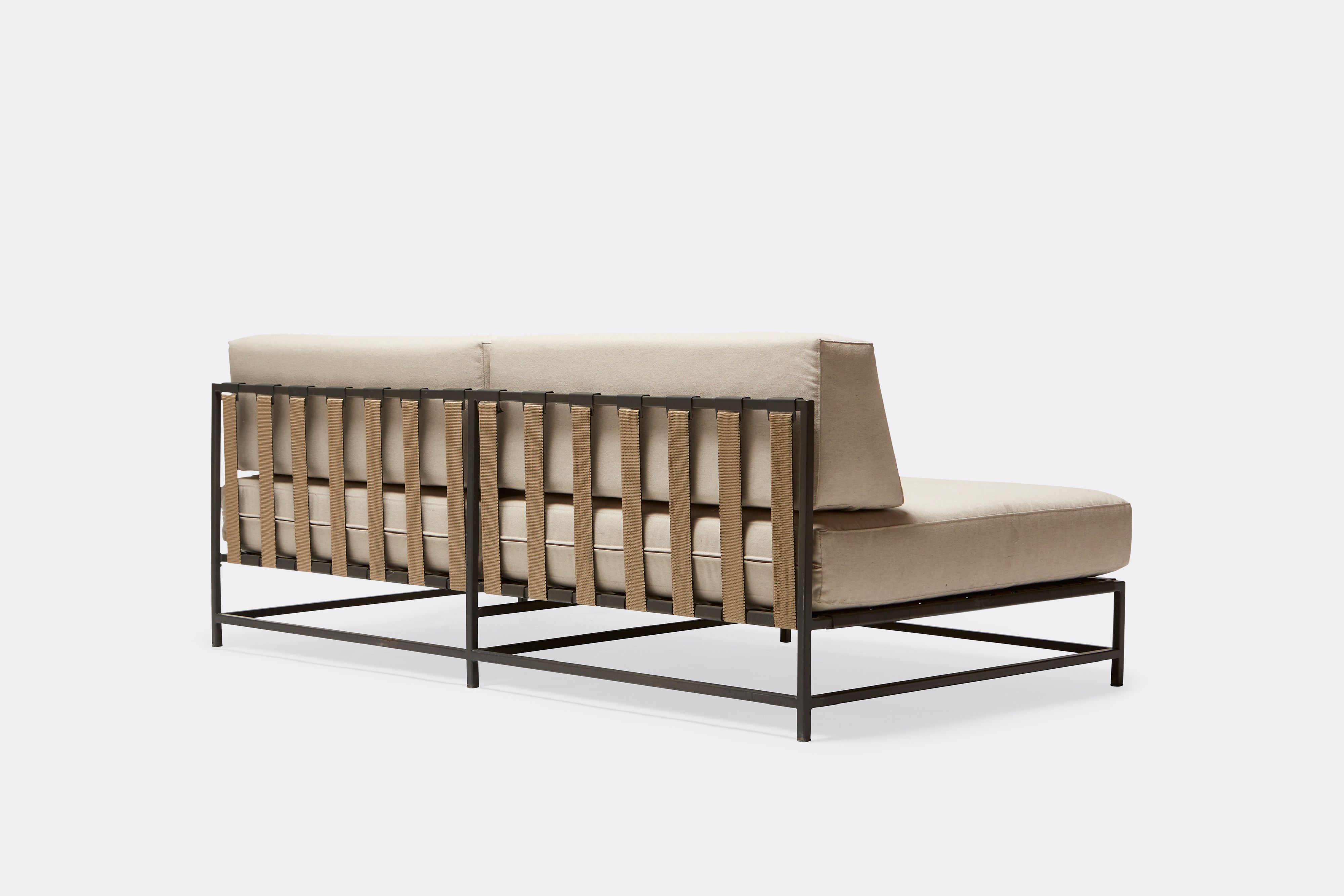 back of outdoor loveseat with cream canvas upholstery and tan belts on dark grey metal frame