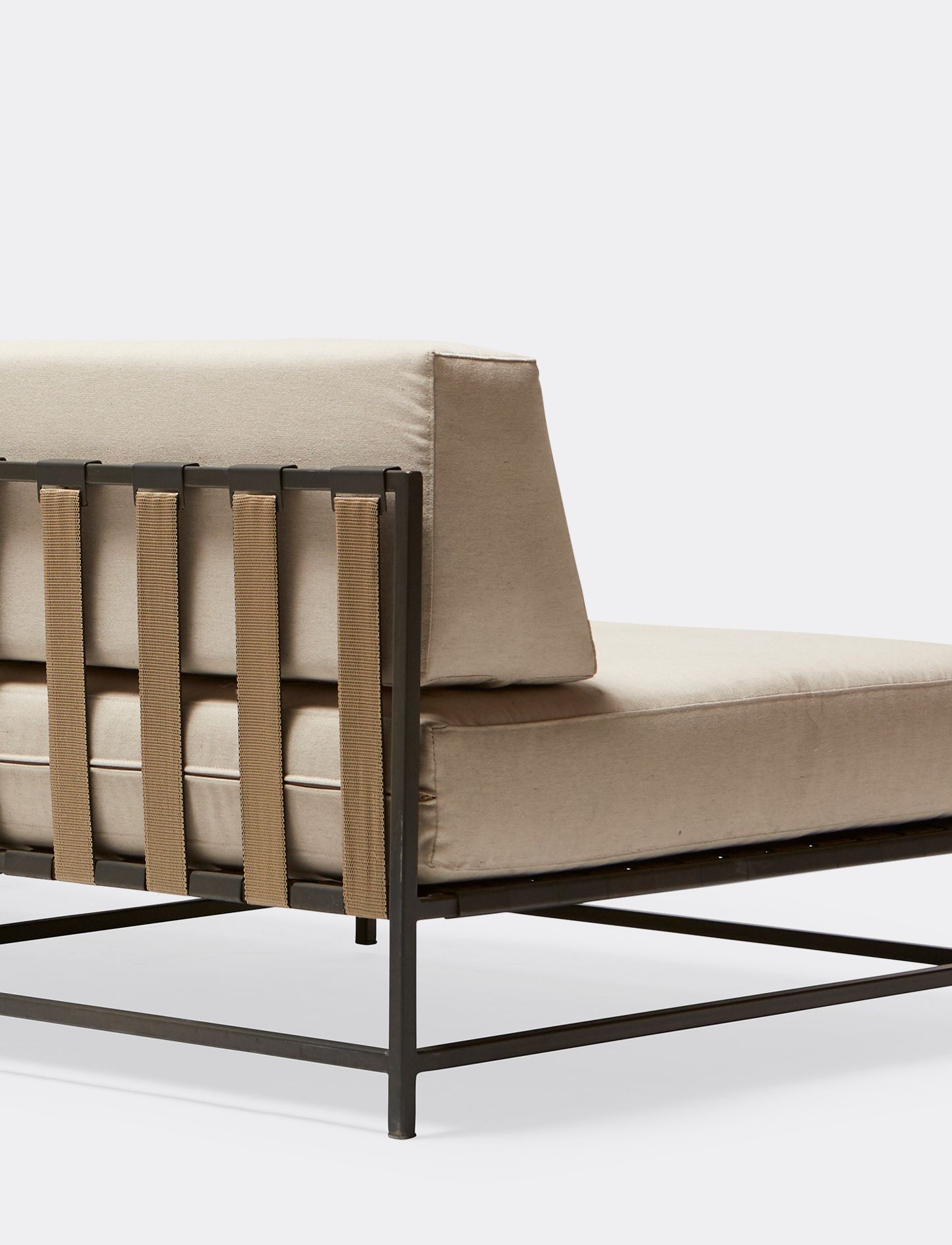 a steel framed sofa with black metal finish and supporting belts and a cream cushion on a white background .