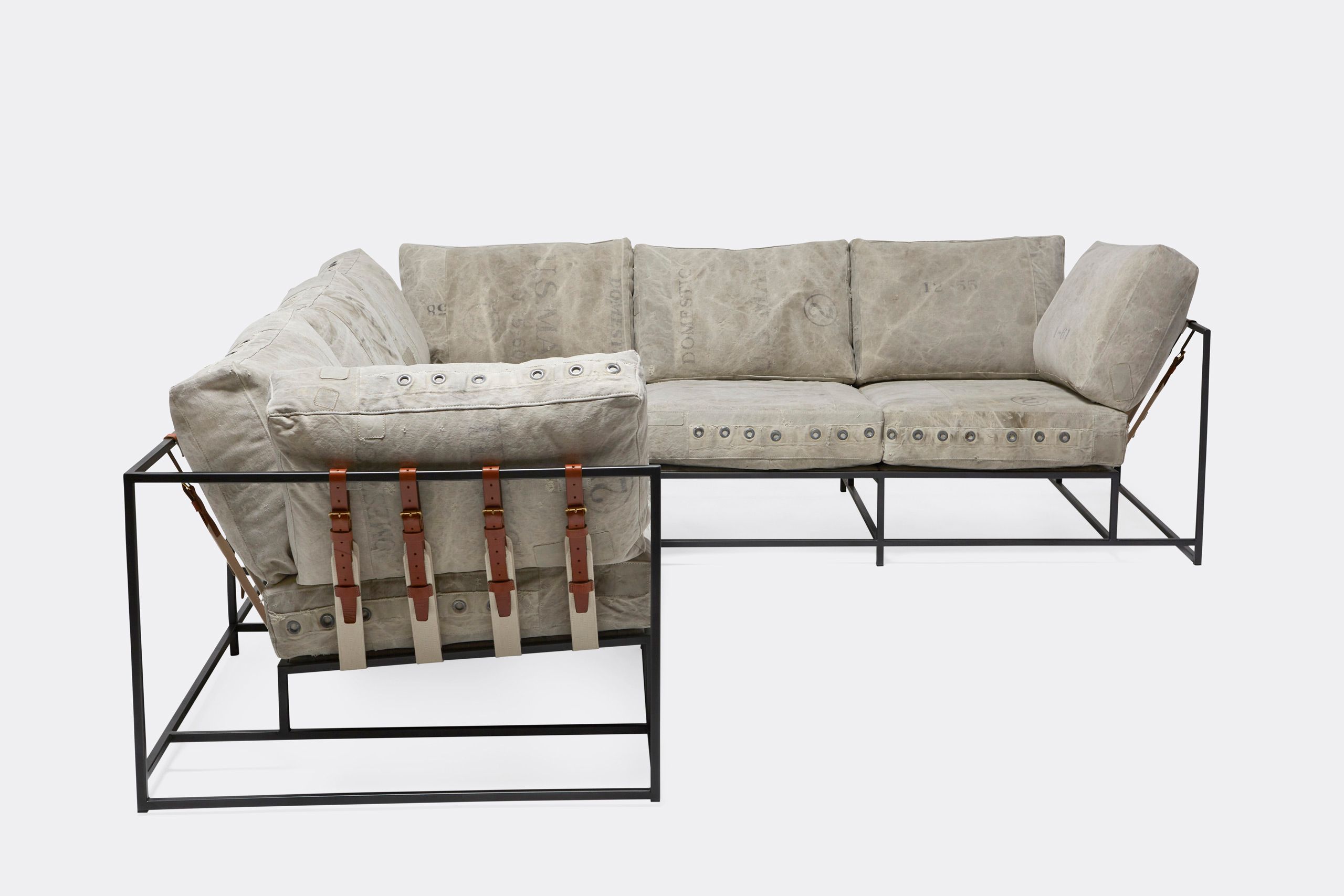 A sofa on with vintage grey canvas covers and leather and webbing straps and on a metal frame shown on a white background