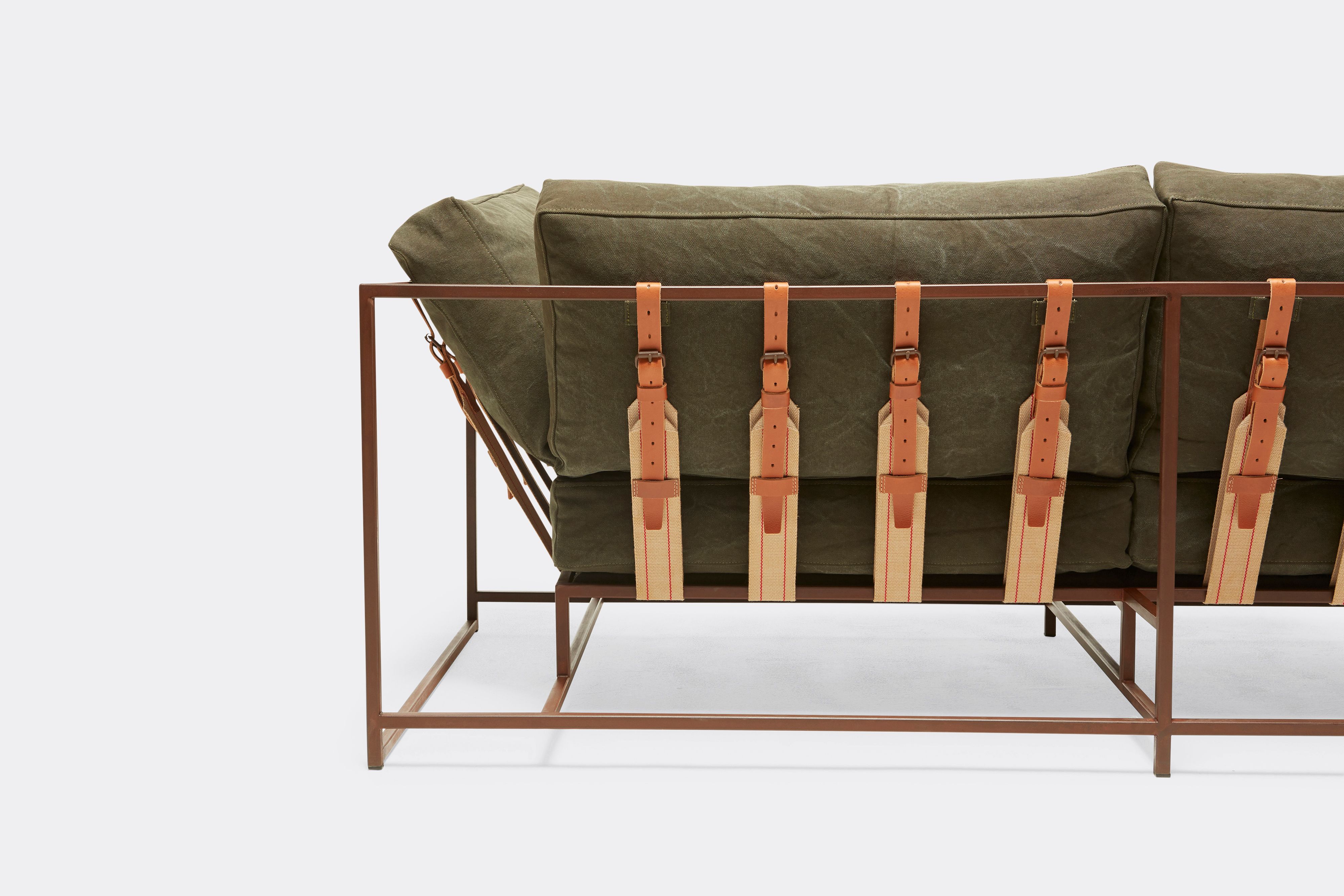 back of two seat sofa with olive canvas upholstery and brown leather belts on marbled rust metal frame