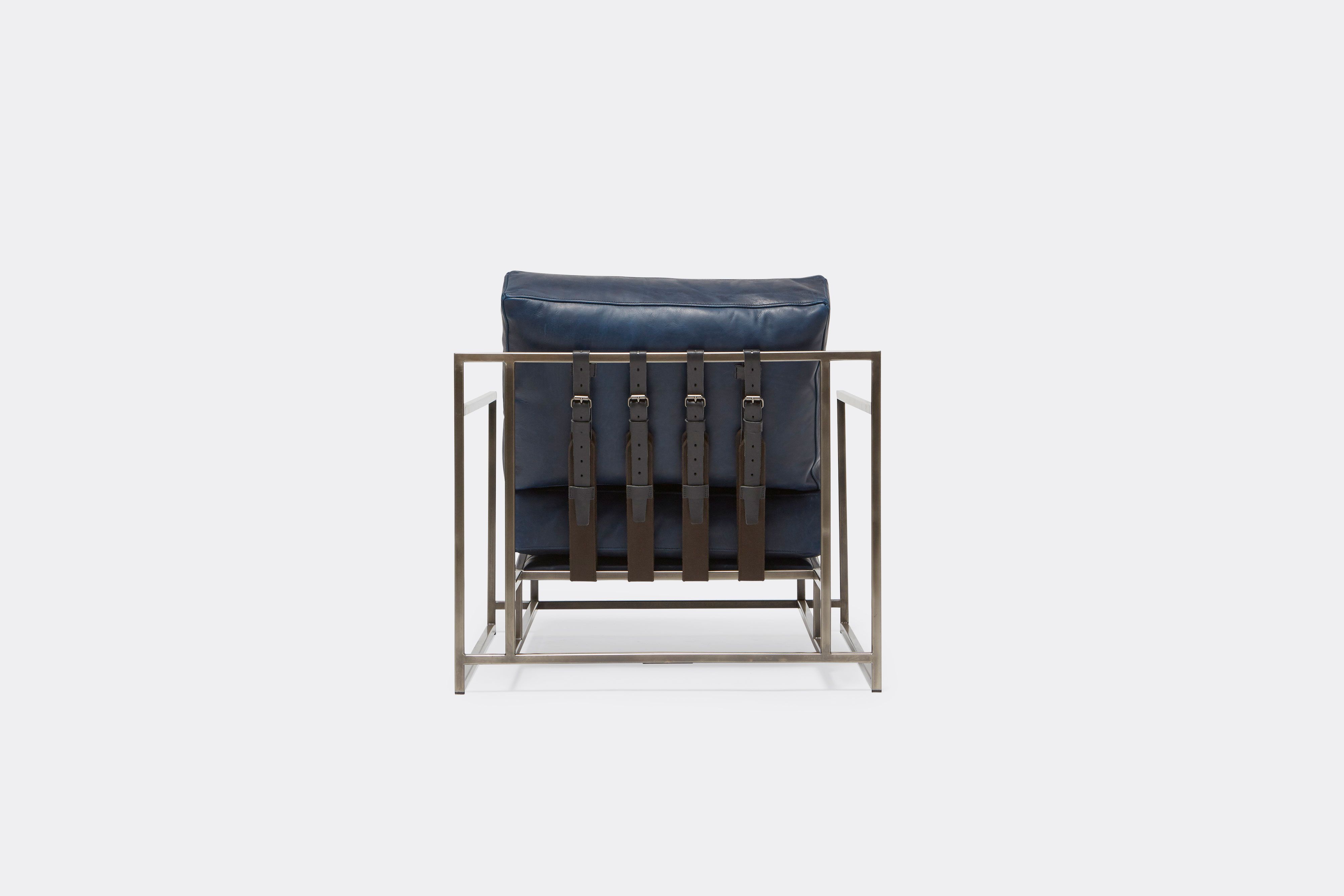 back of armchair with blue leather upholstery and black leather belts on antique nickel metal frame