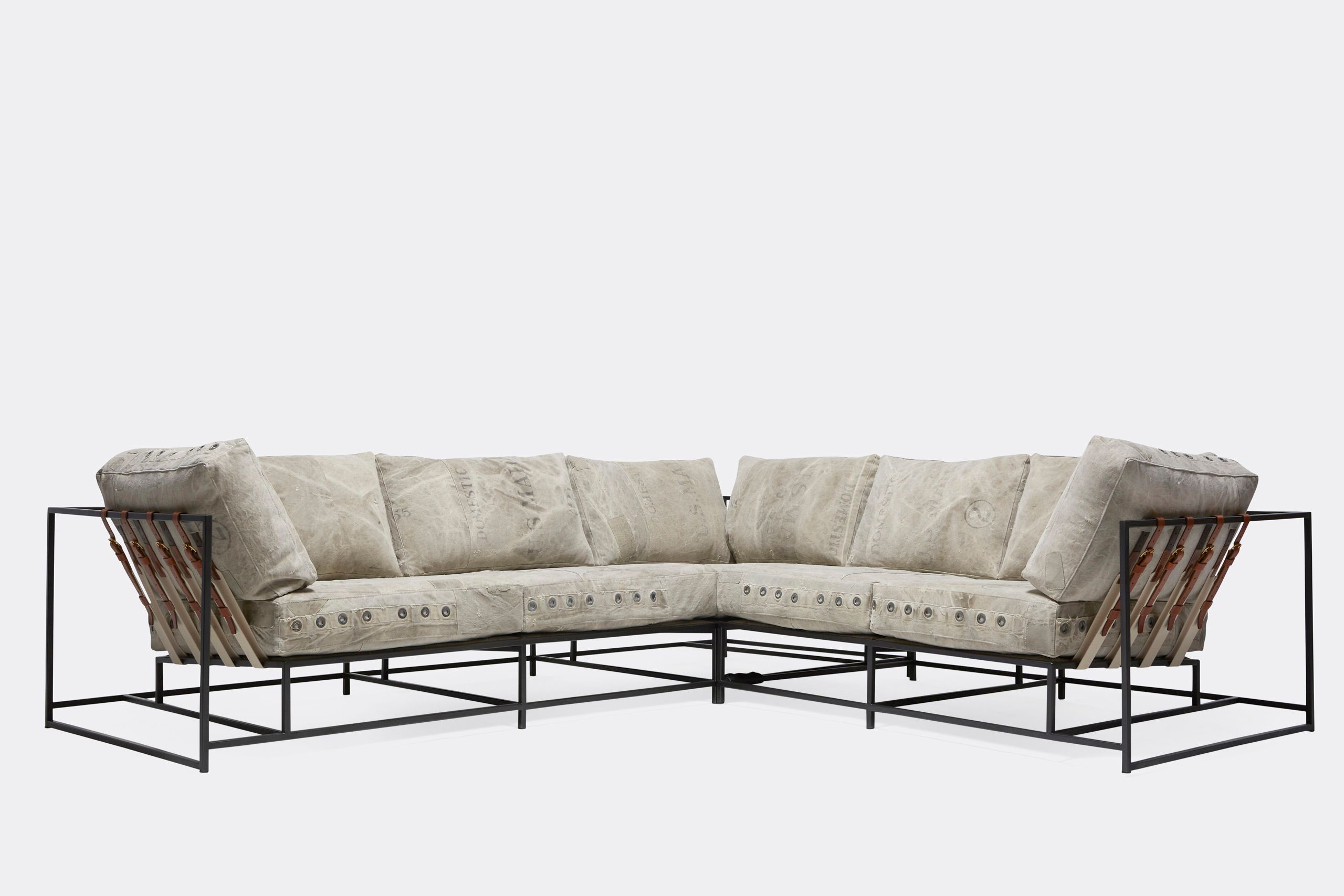 A sofa on with vintage grey canvas covers and leather and webbing straps and on a metal frame shown on a white background