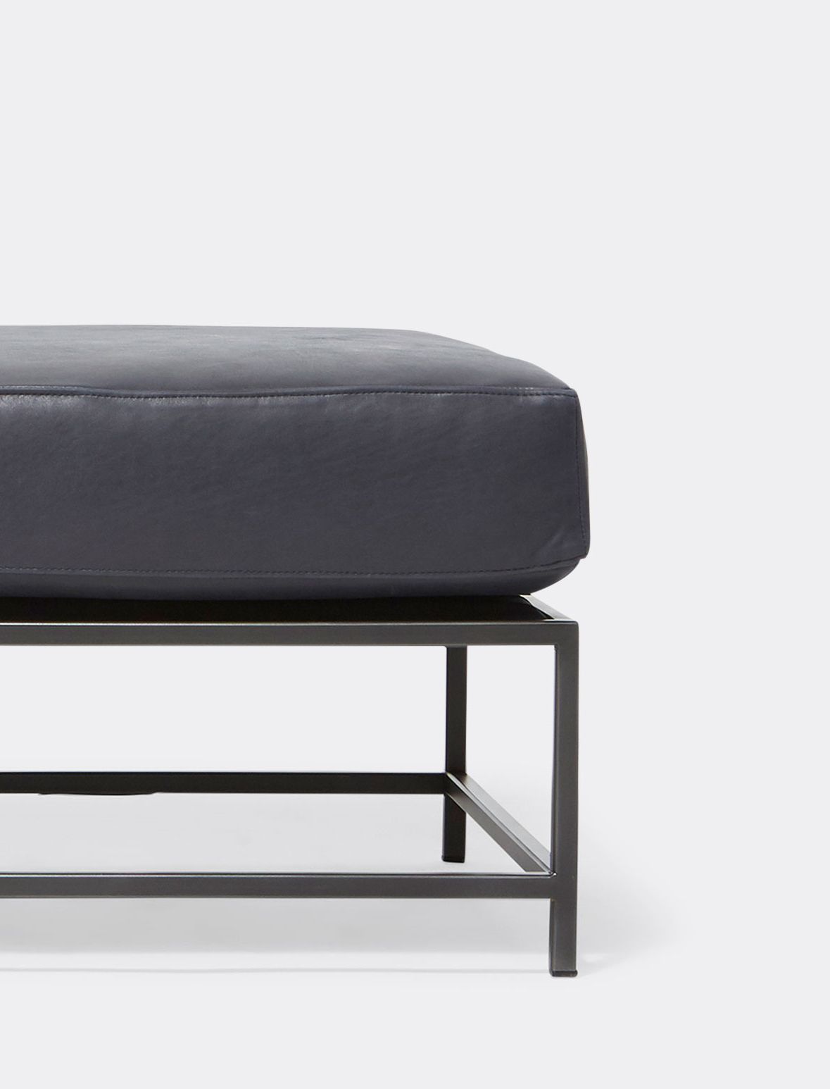 a dark blue leather bench with a black metal frame shown on a white background .
