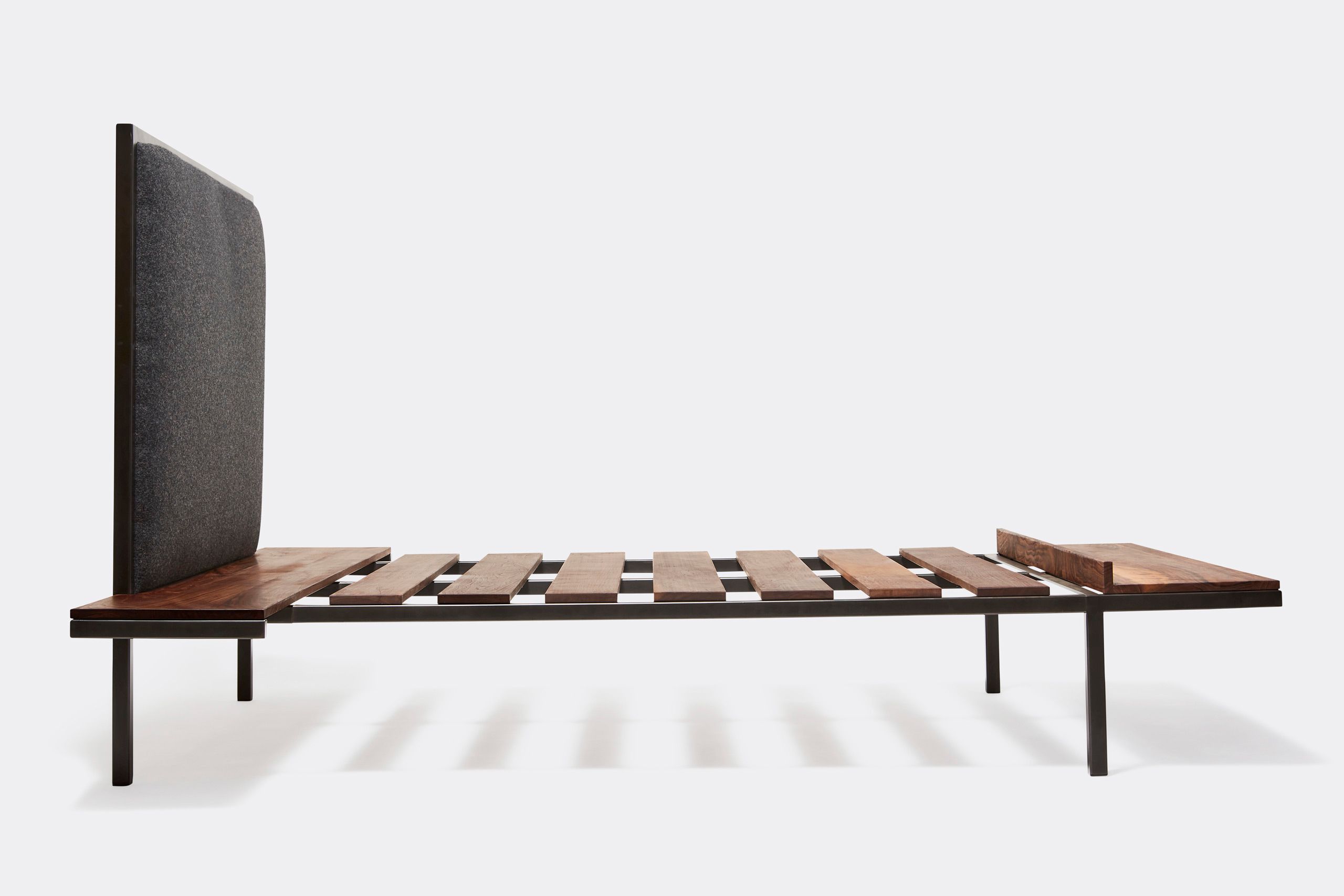 a steel frame and walnut wood bed with a black wool upholstered headboard shown on a white background .