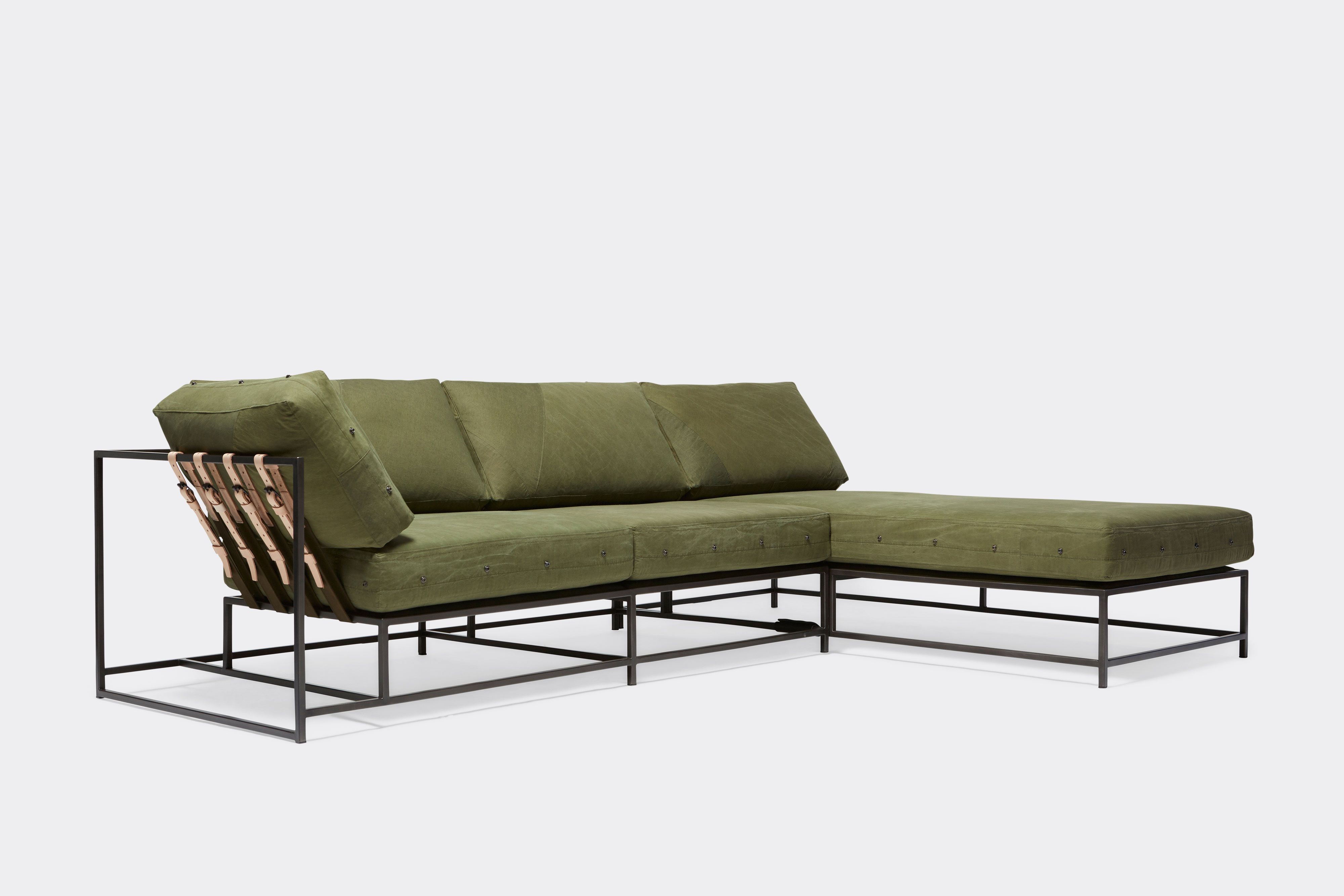side of sectional with green canvas upholstery and natural tan leather belts on black metal frame