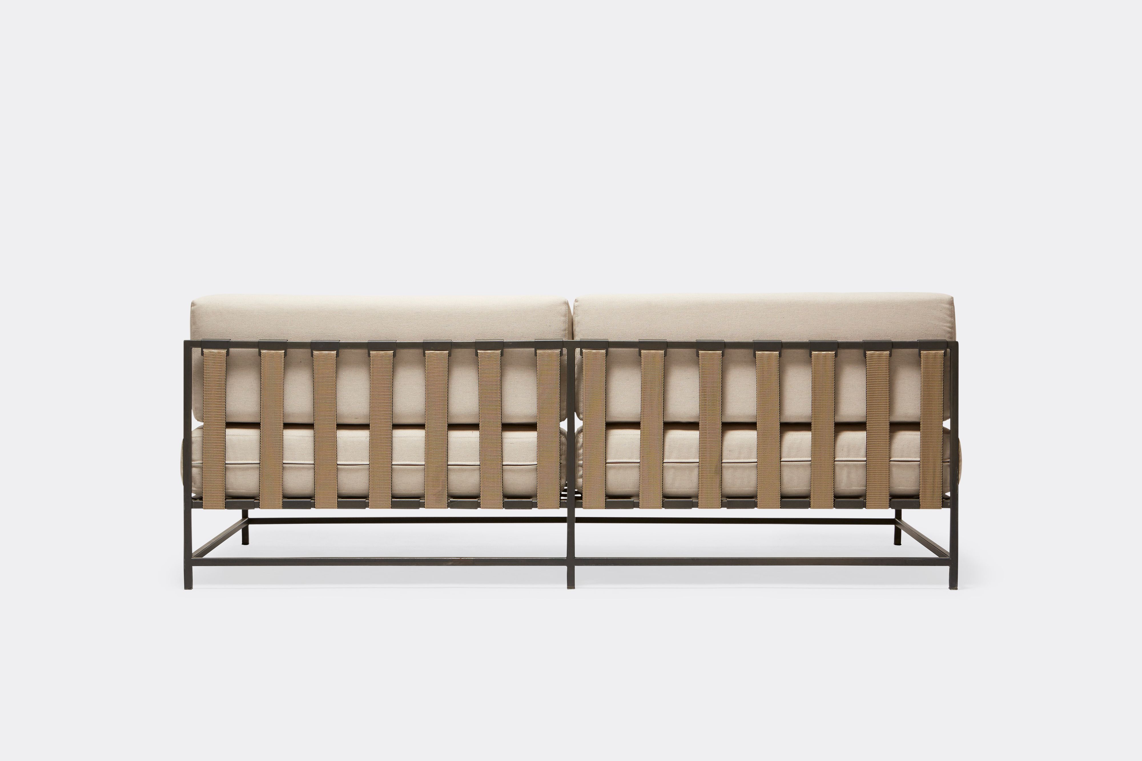 back of outdoor loveseat with cream canvas upholstery and tan belts on dark grey metal frame