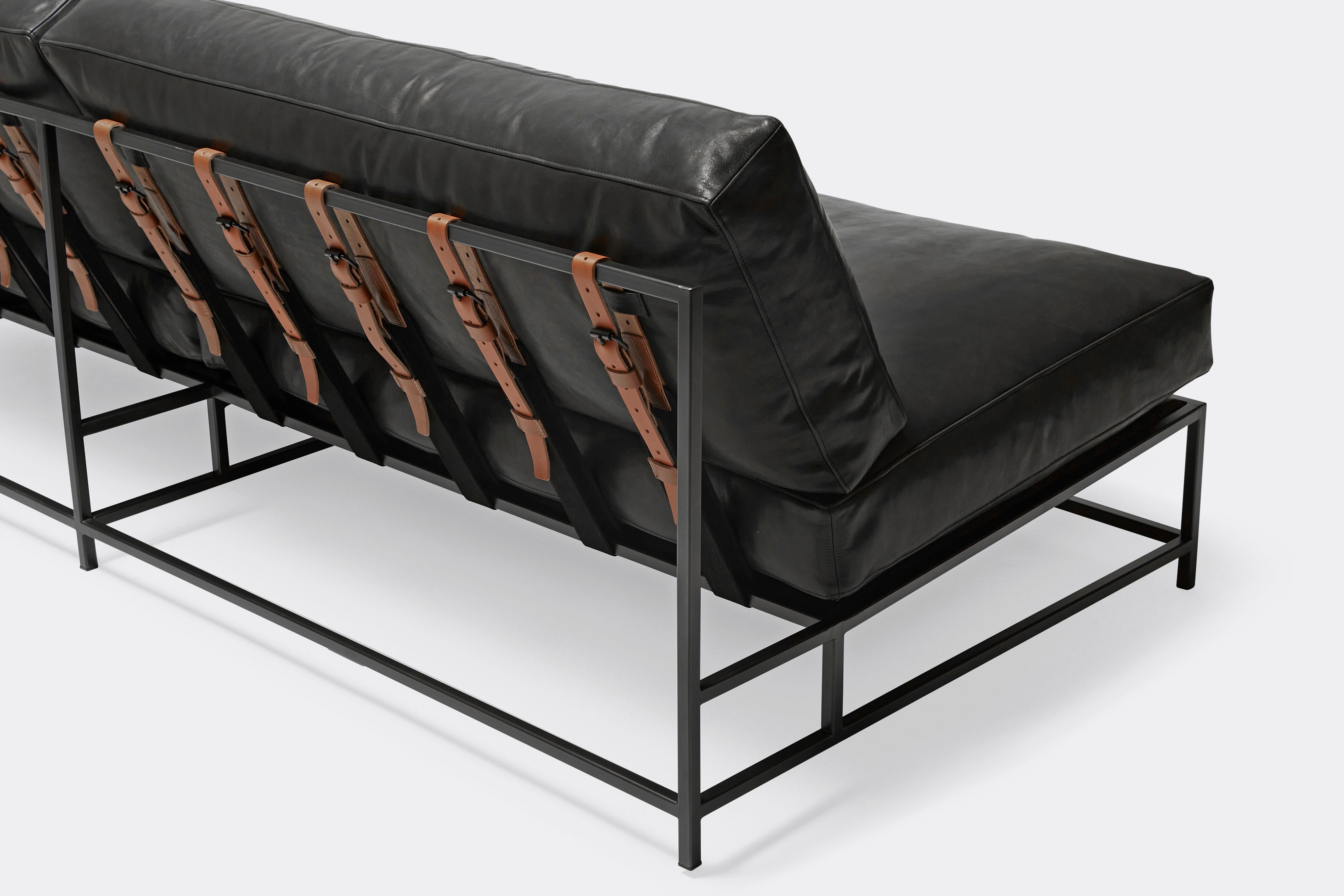 overhead of loveseat with black leather upholstery and brown leather belts on black metal frame