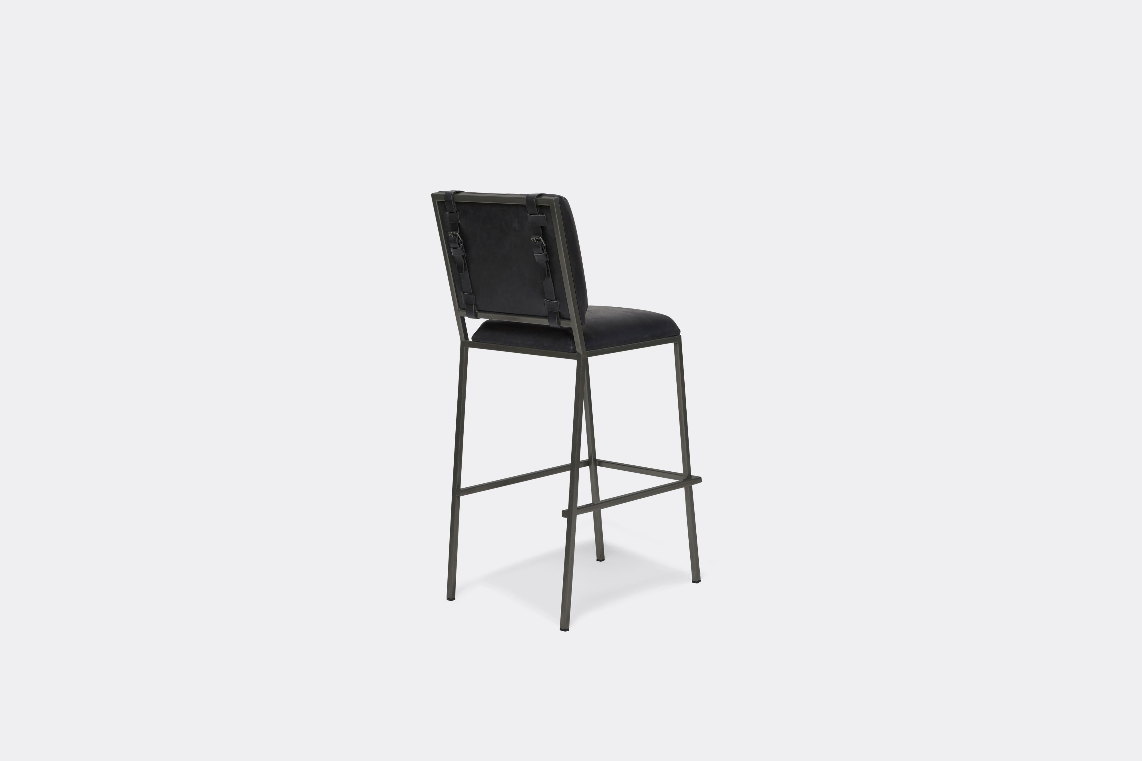 Back of barstool with black leather upholstery and black leather belts on blackened steel metal legs