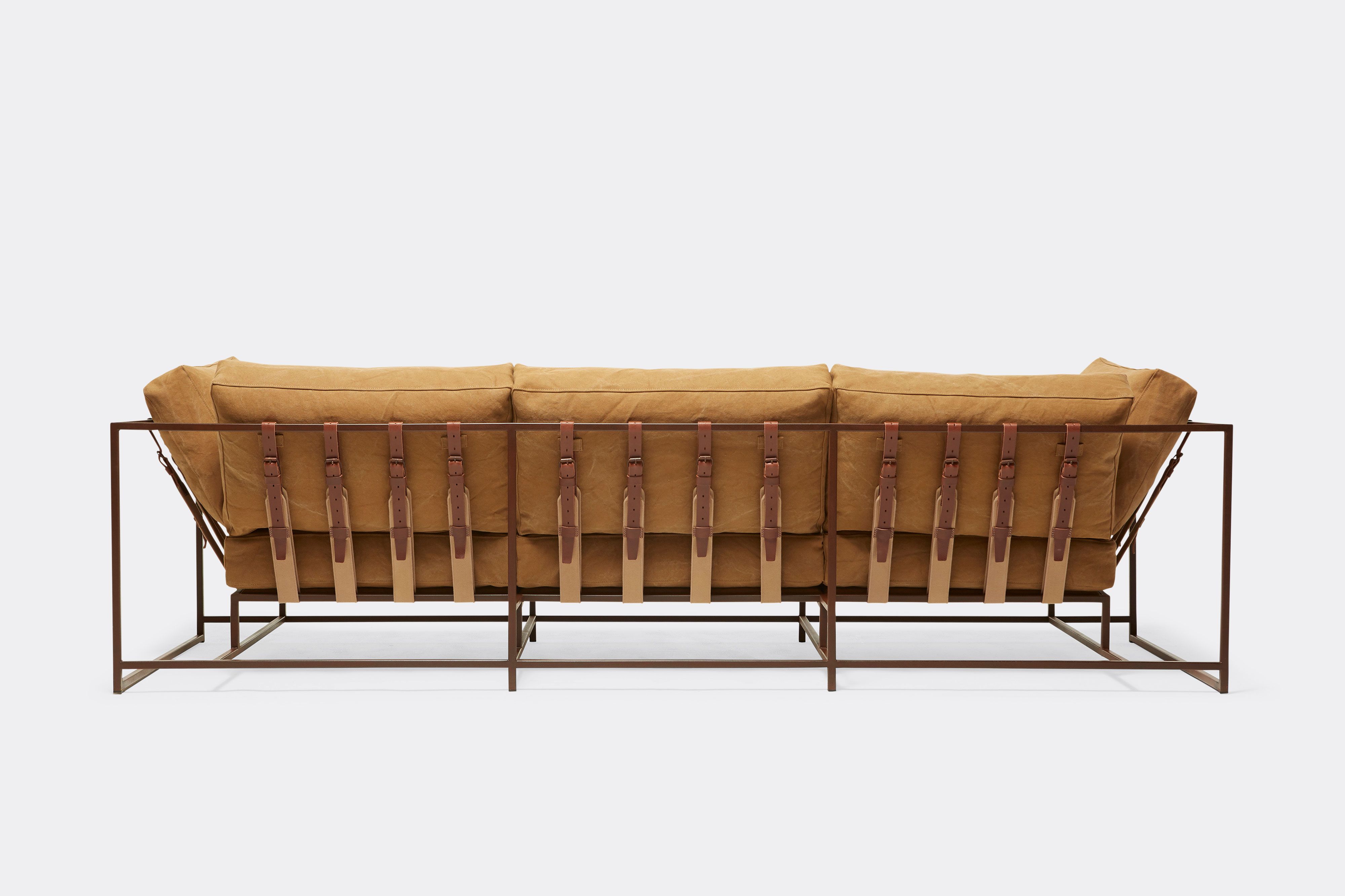 back of sofa with tan canvas upholstery and brown leather belts on marble rust metal frame