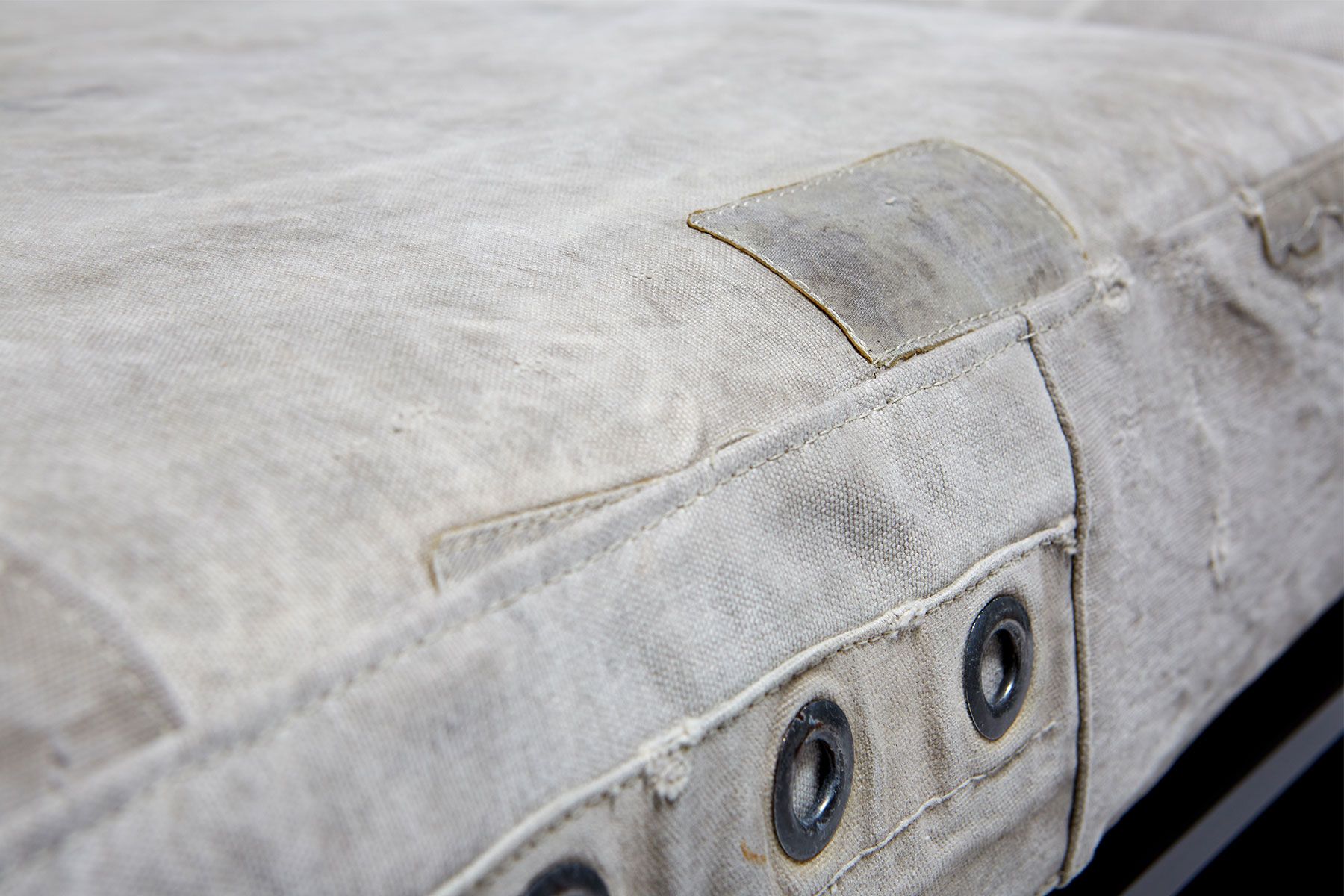 A sofa on with vintage grey canvas covers and leather and webbing straps and on a metal frame shown on a white background