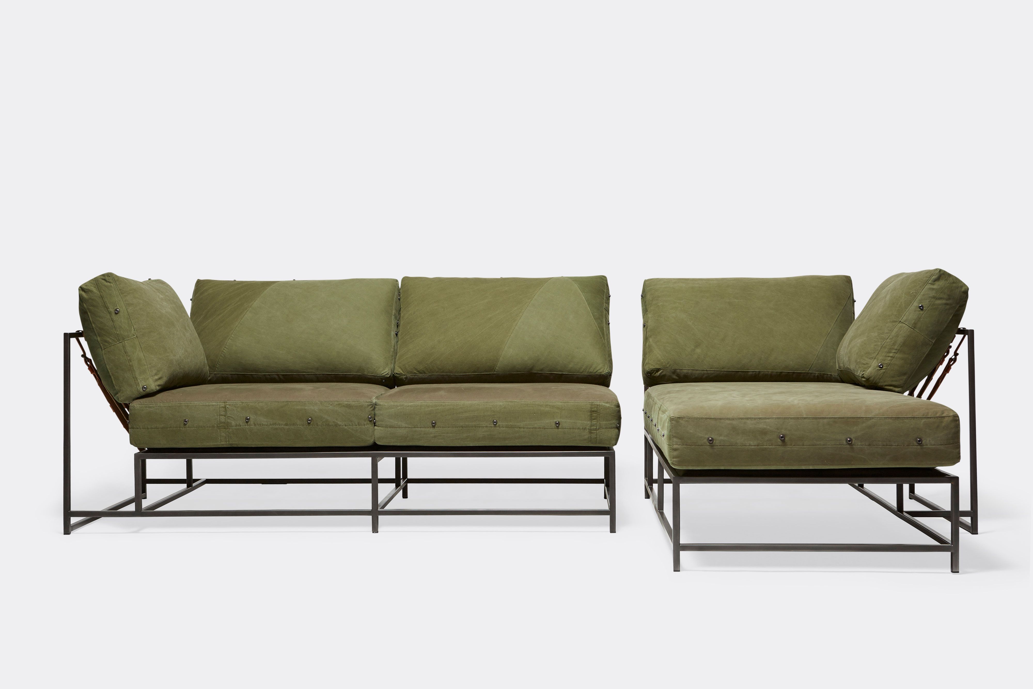 a sofa with green cushions and a metal frame and tan leather and webbing belts on a white background .