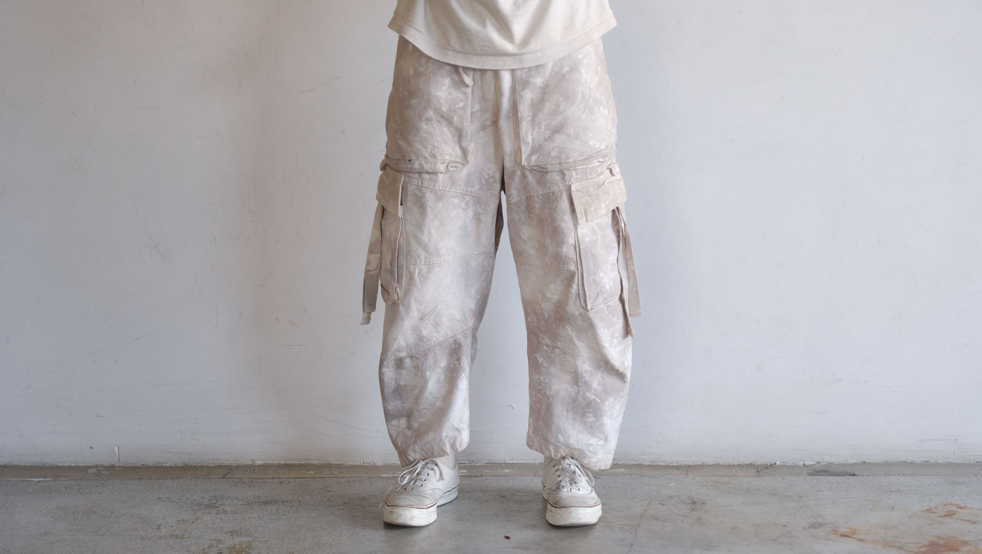Mottled beige cargo pants with large side pockets and hanging straps, worn with platform sneakers.