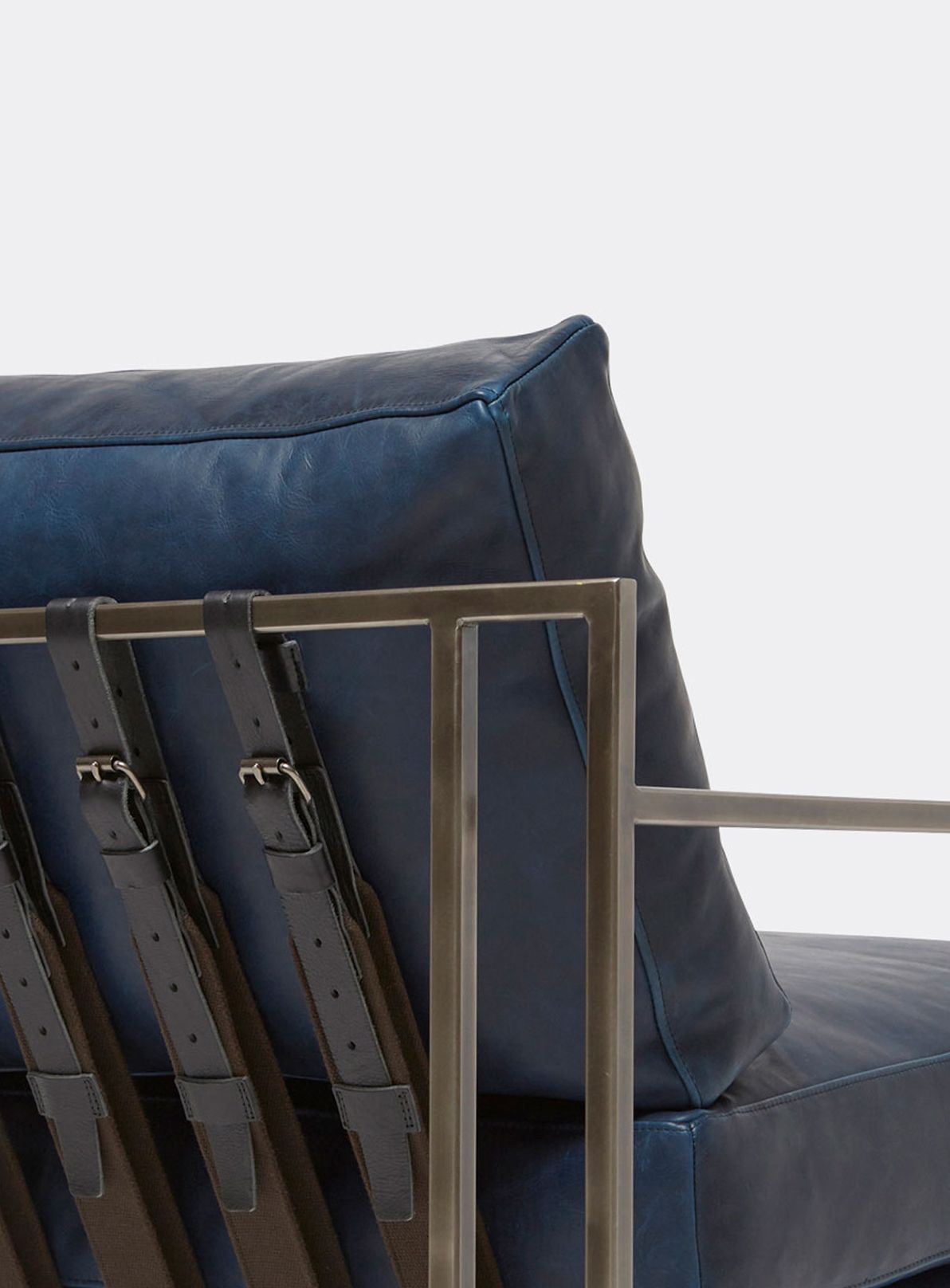 a navy blue leather armchair with a black steel frame and black supporting belts shown on a white background .