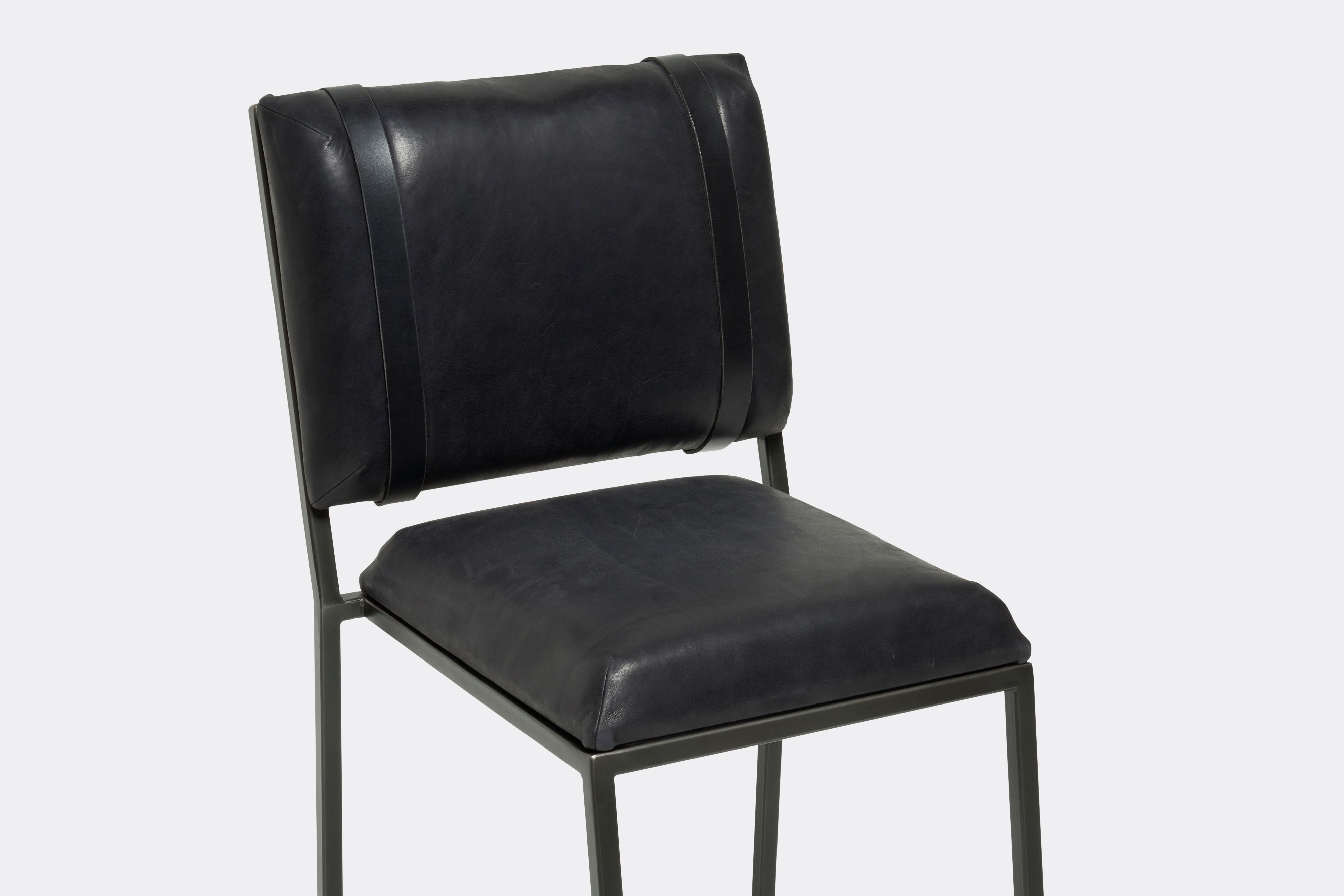 Detail of barstool with black leather upholstery and black leather belts on blackened steel metal legs