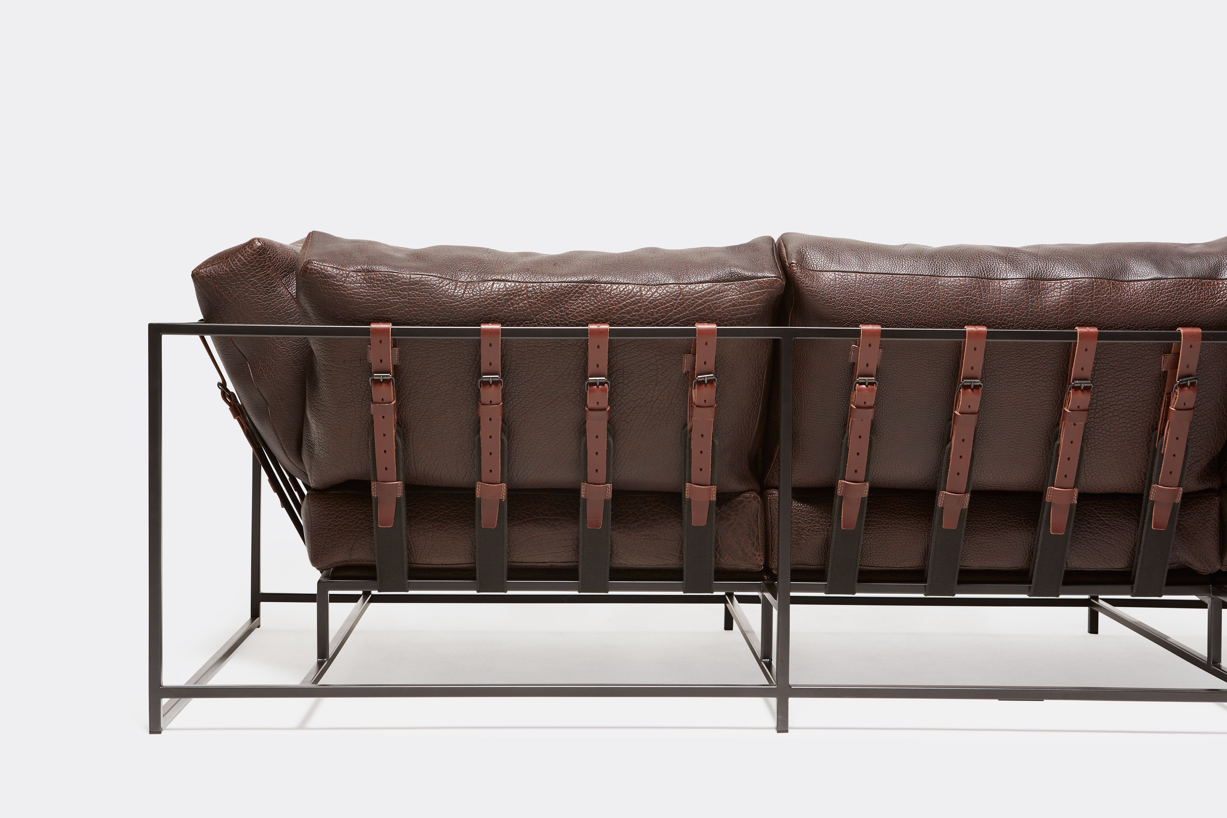 Up close, back view of brown leather sofa with blacken steel metal frame and leather belts.