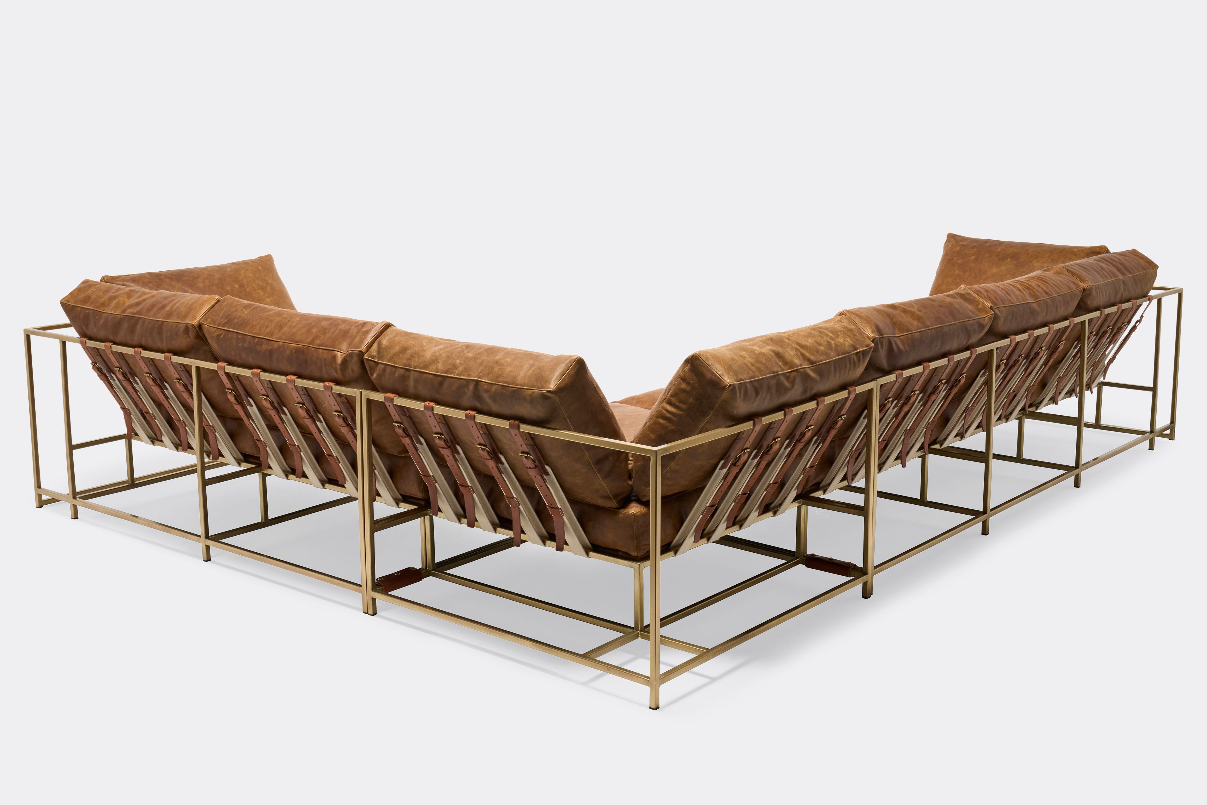 back of sectional with tan leather upholstery and brown leather belts on antique brass metal frame