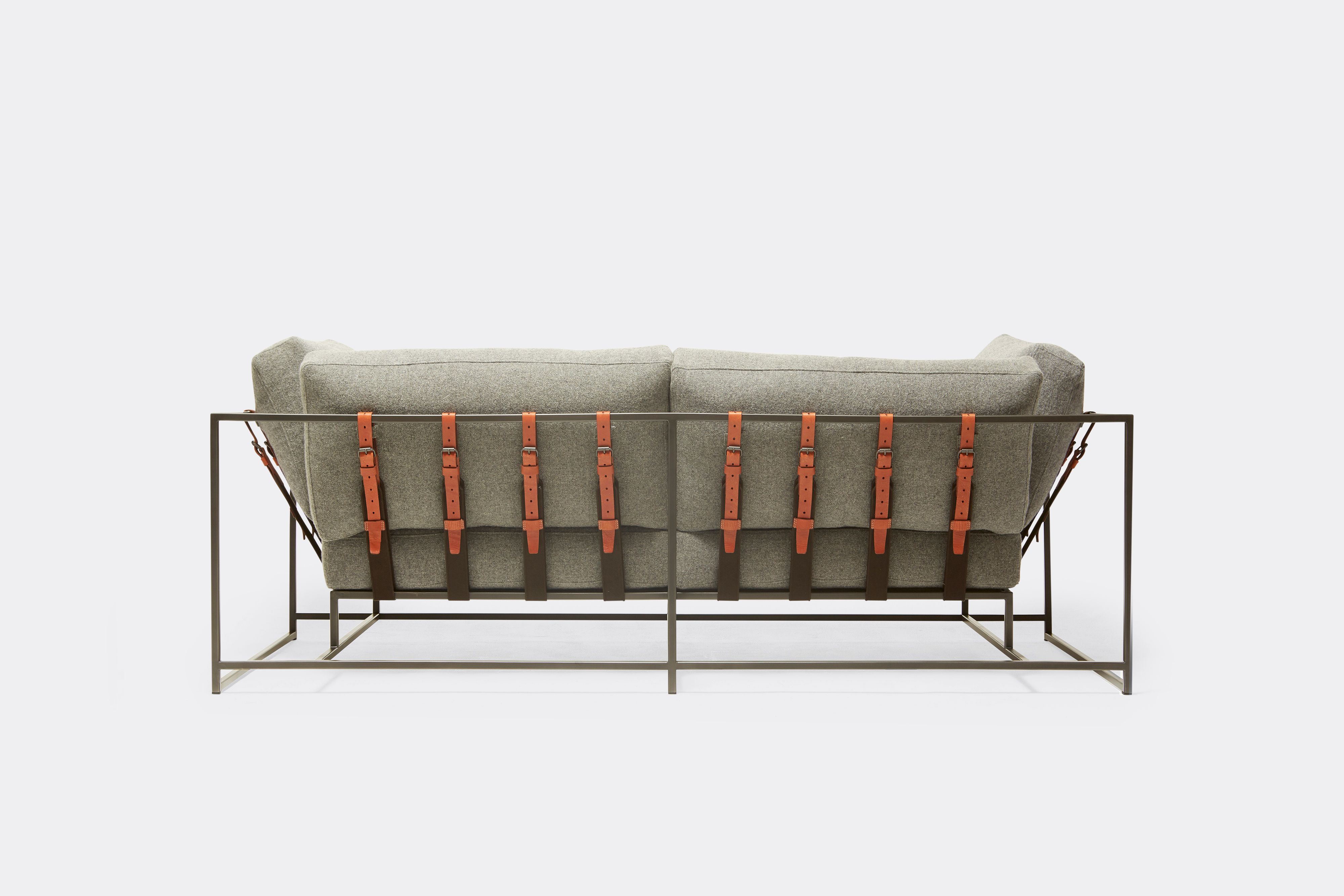 Back of two seat sofa with grey wool upholstery and brown leather belts on black metal frame