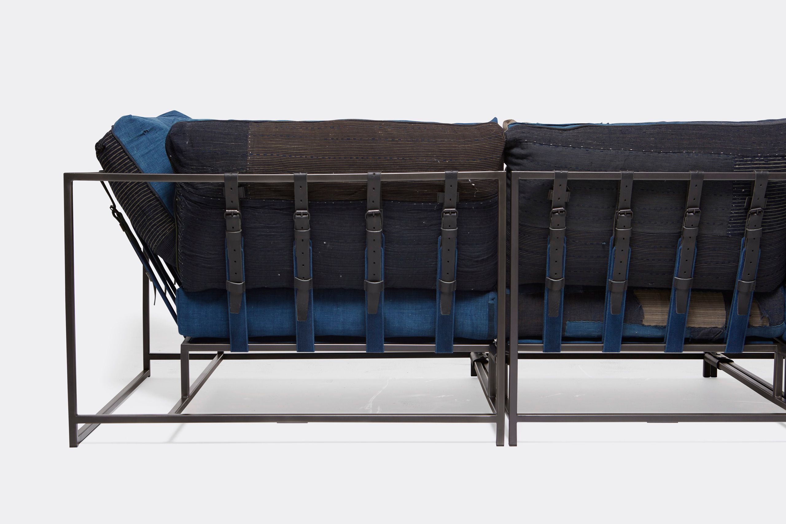 A steel framed sofa with vintage Japanese indigo and grey upholstery and supporting belts shown on a white background