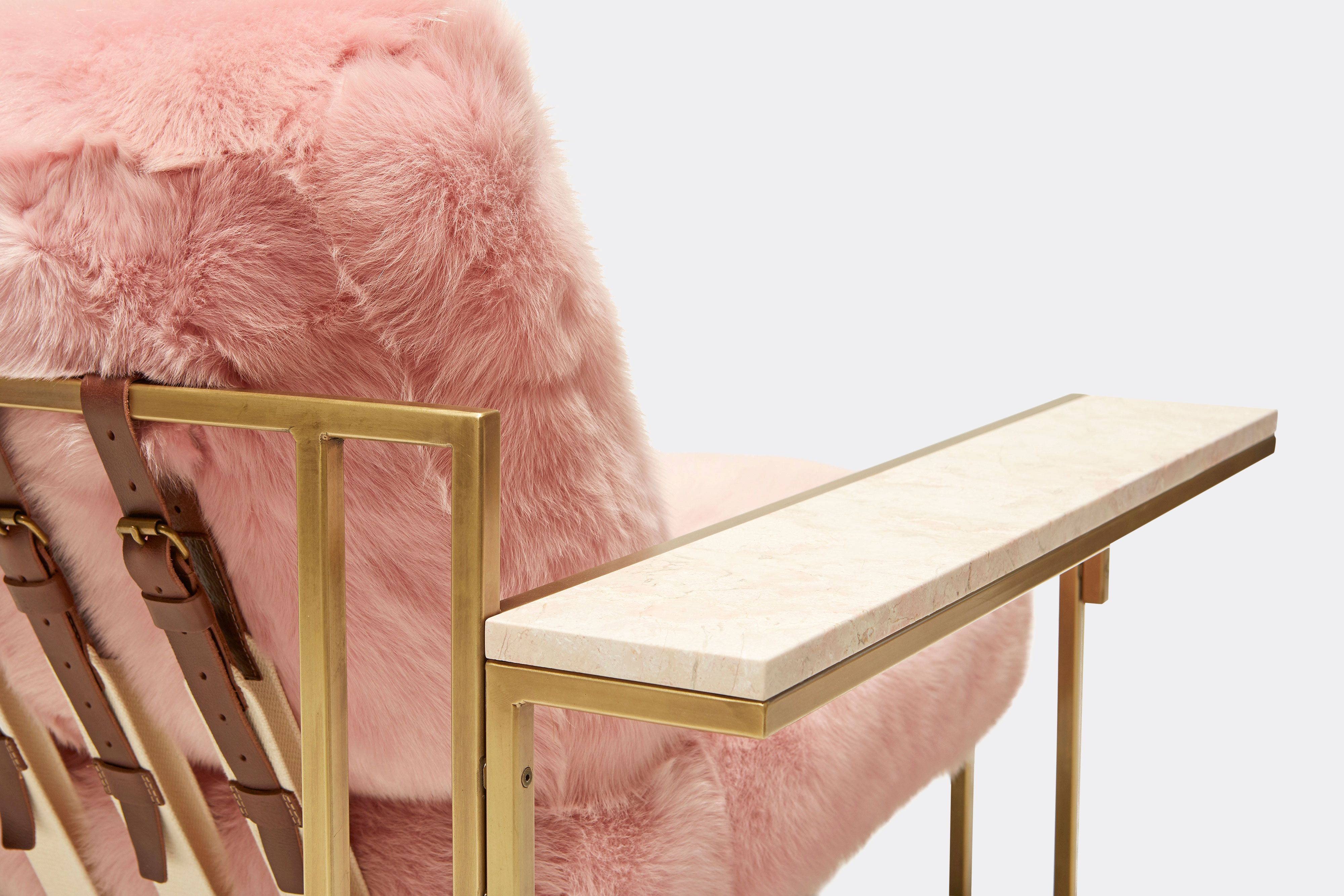 detail of armchair with pink shearing upholstery and brown leather belts on antique brass metal frame
