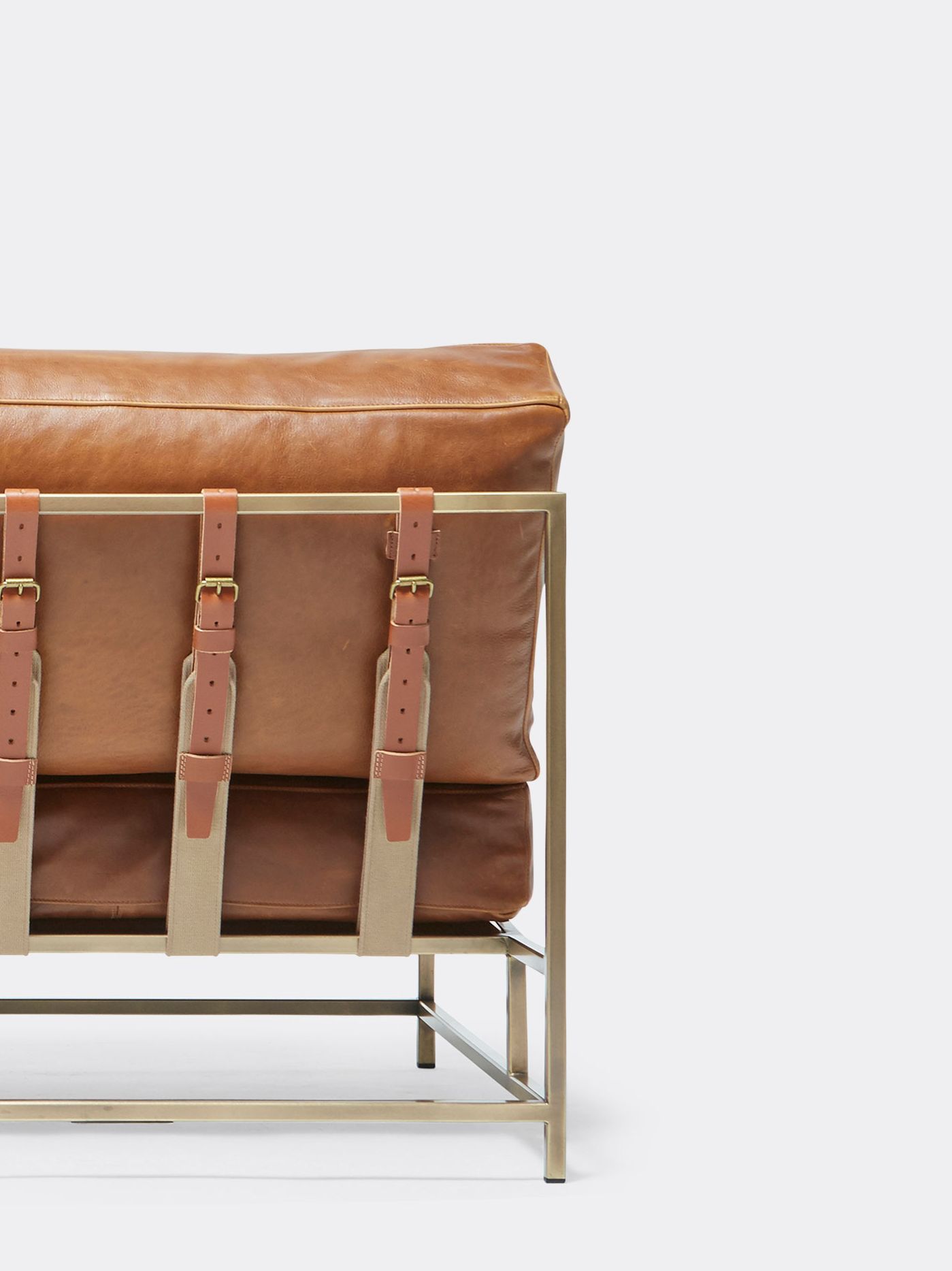 a brown leather couch with a brass metal frame and supporting belts shown on a white background .