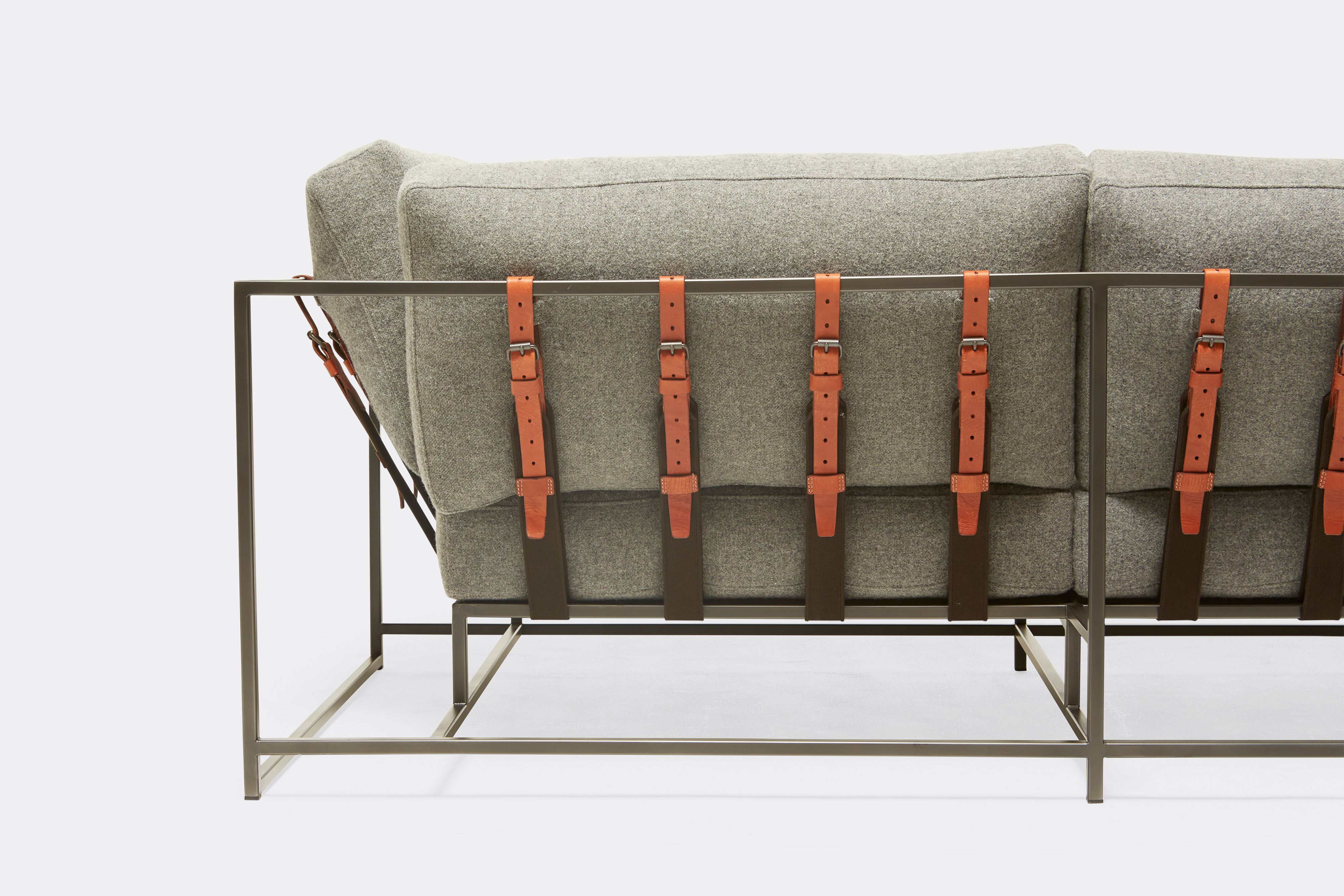 Back of two seat sofa with grey wool upholstery and brown leather belts on black metal frame