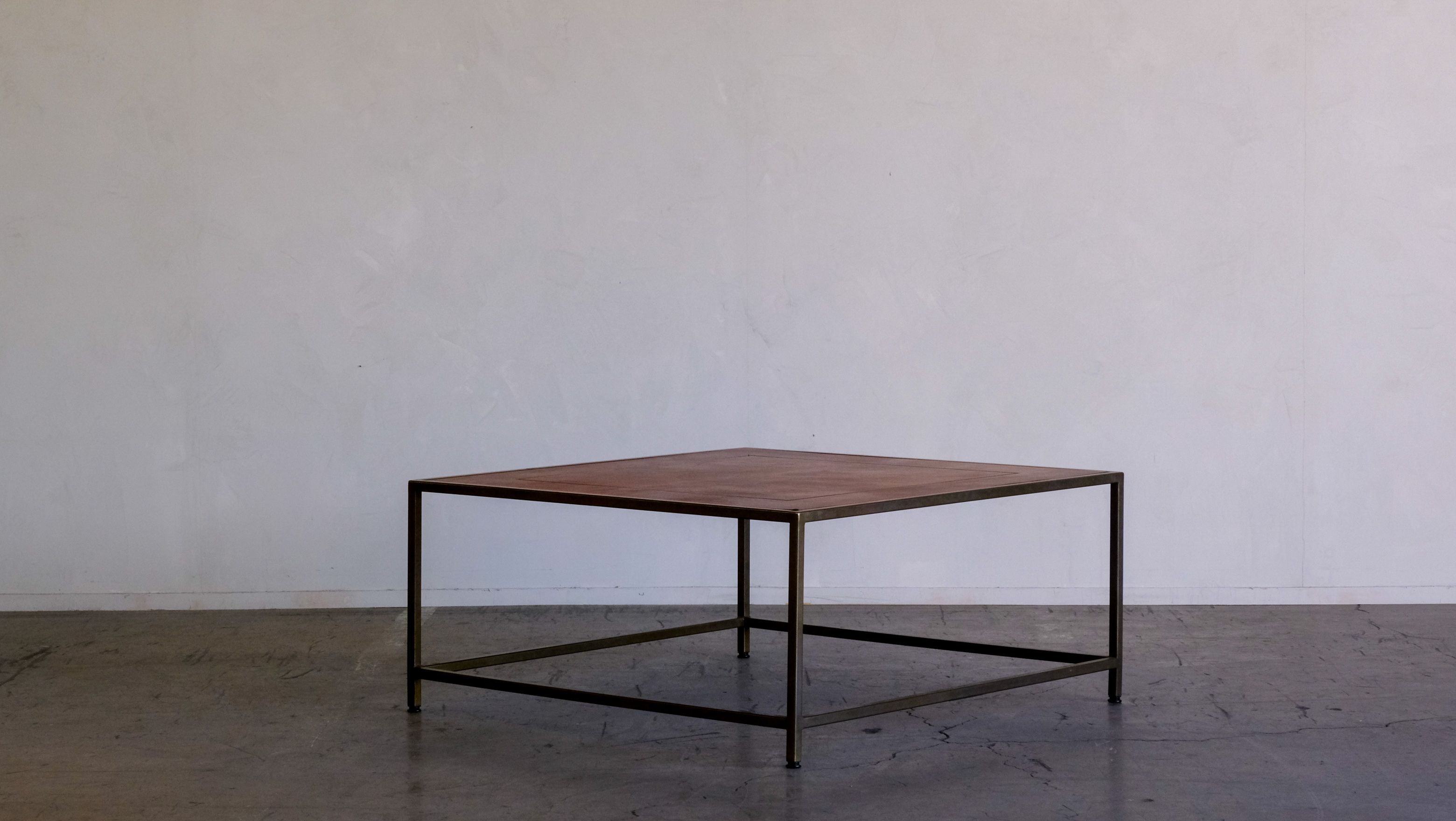 a square coffee table with a leather top and a metal frame is sitting on a concrete floor in front of a white wall .