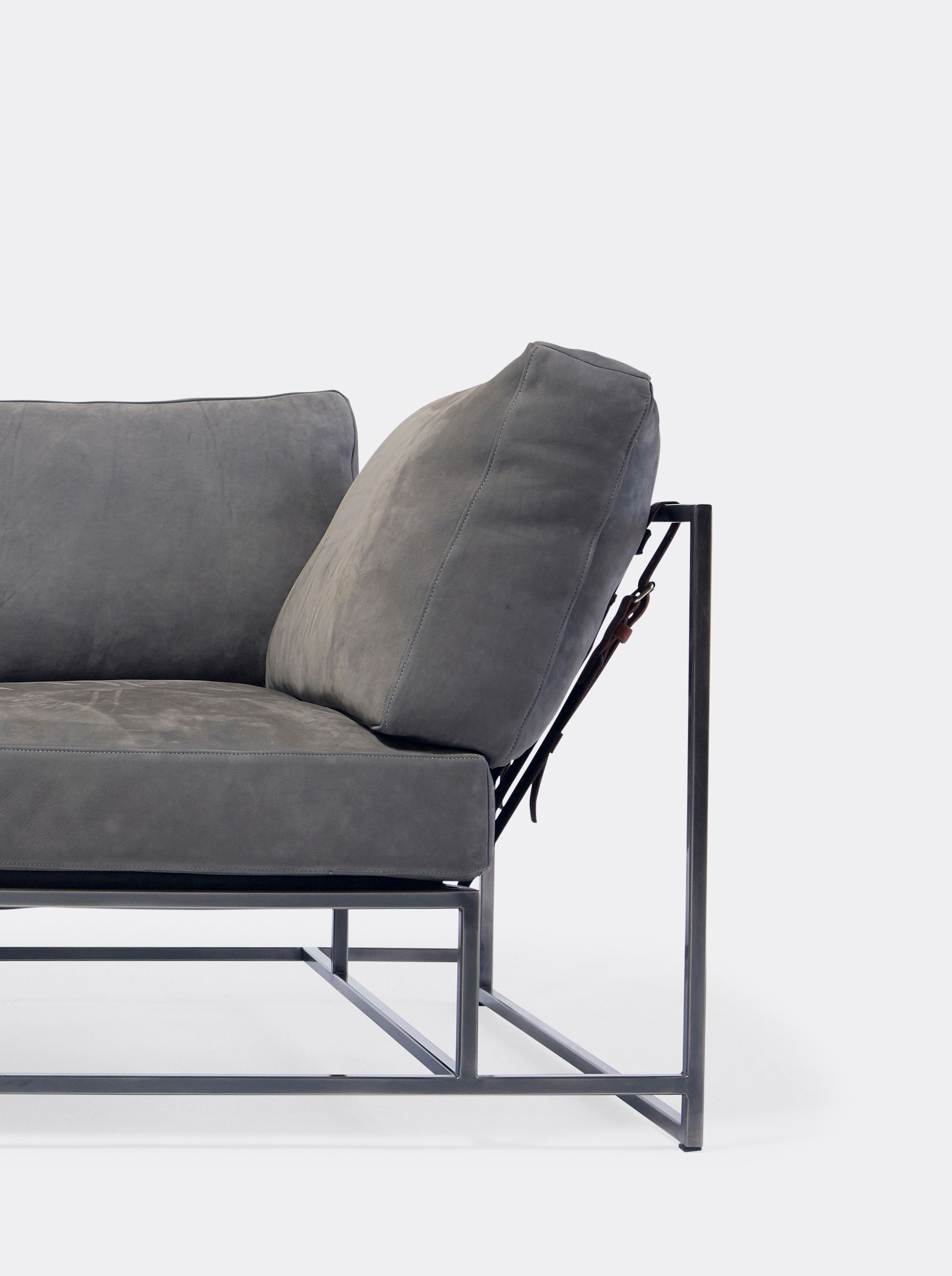 a grey leather sofa with a metal frame and supporting belts is sitting on a white background .