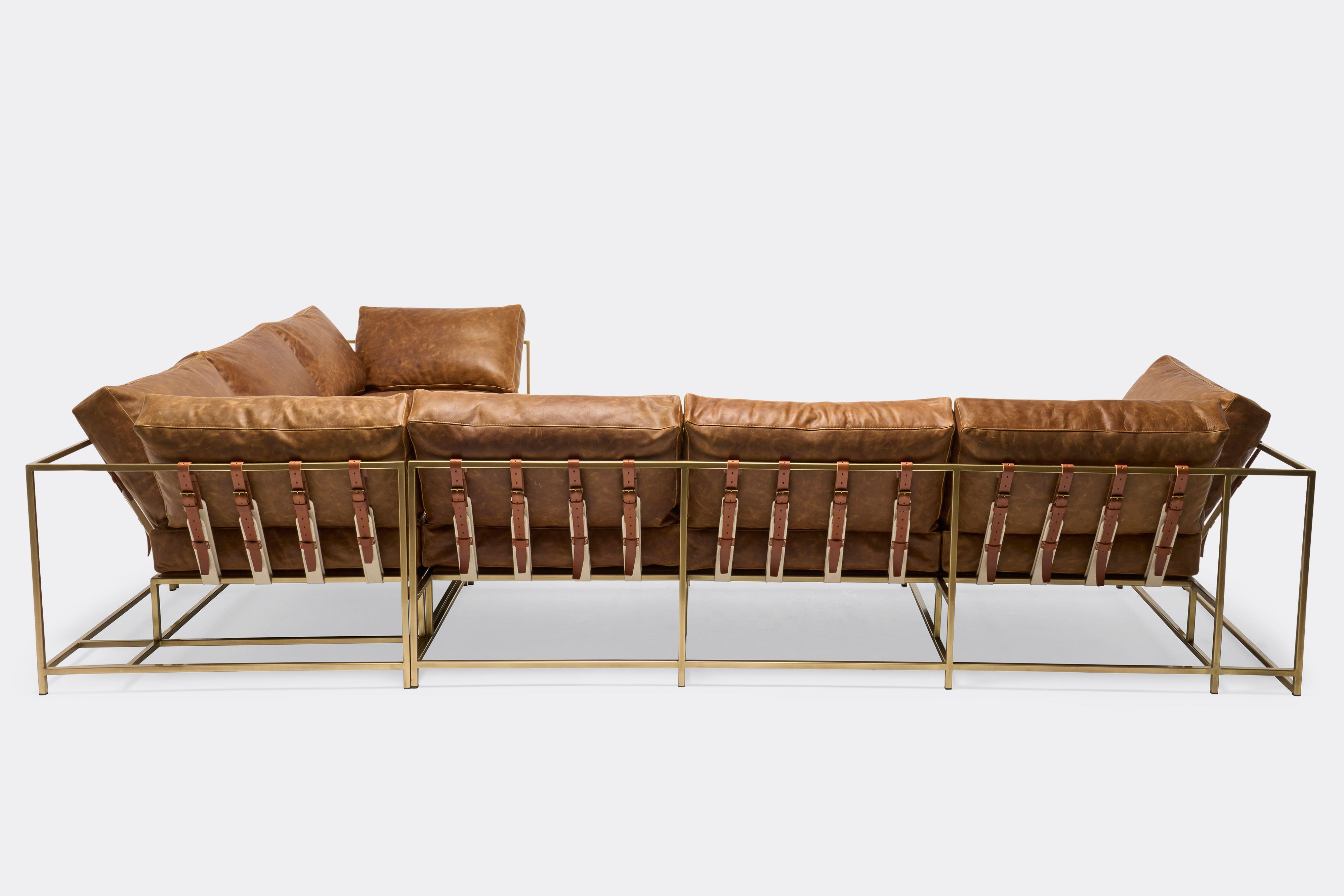 back of sectional with tan leather upholstery and brown leather belts on antique brass metal frame