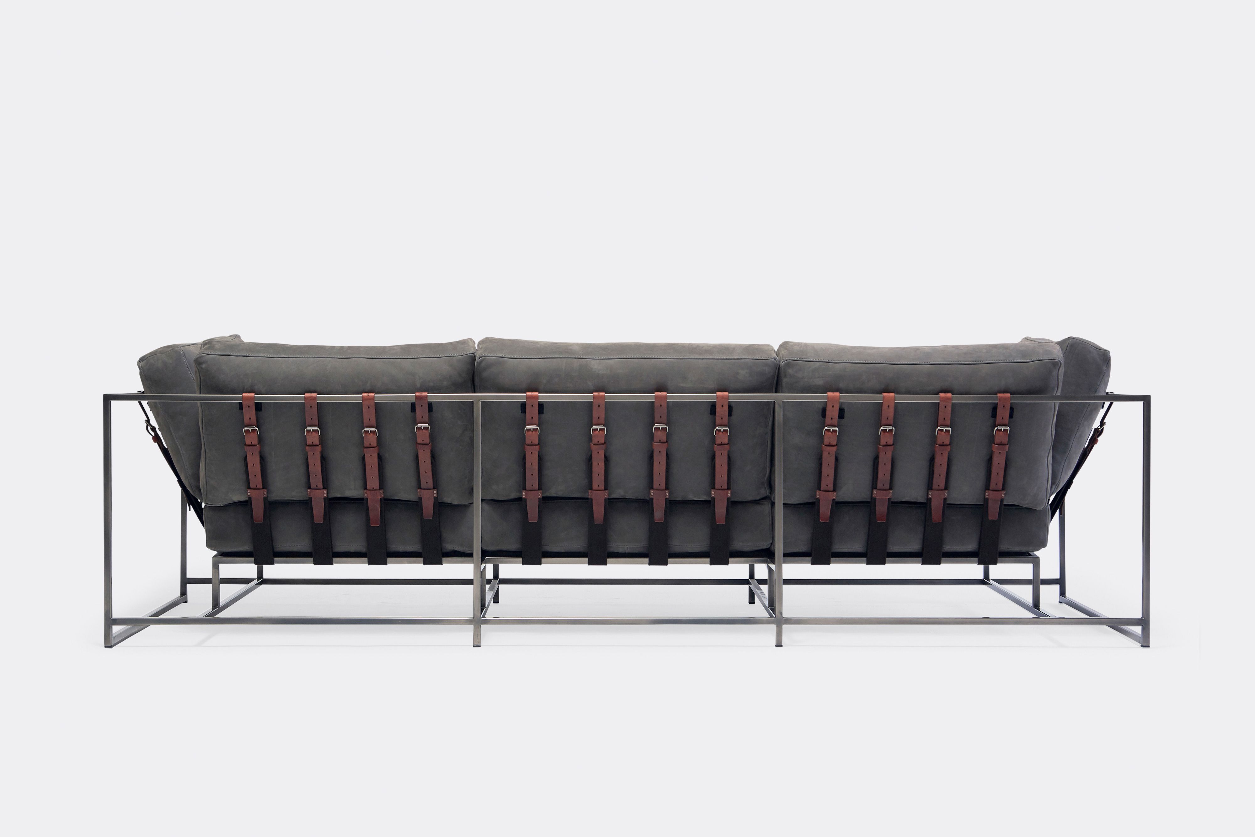 Back of sofa with grey leather upholstery and brown leather belts on antique nickel metal frame