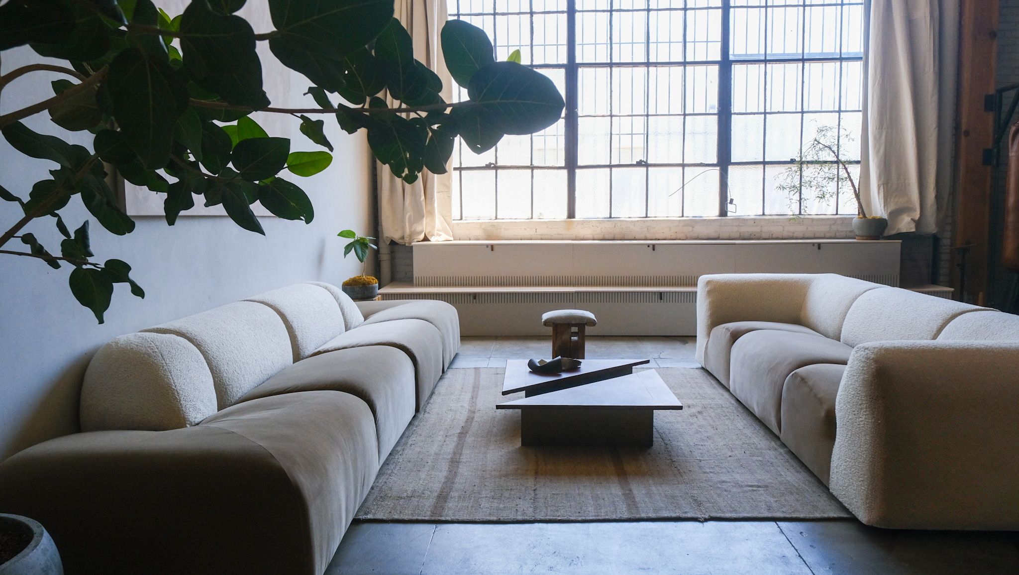 Two beige and white modular sofas face a coffee table in a modern living room with a large grid window.