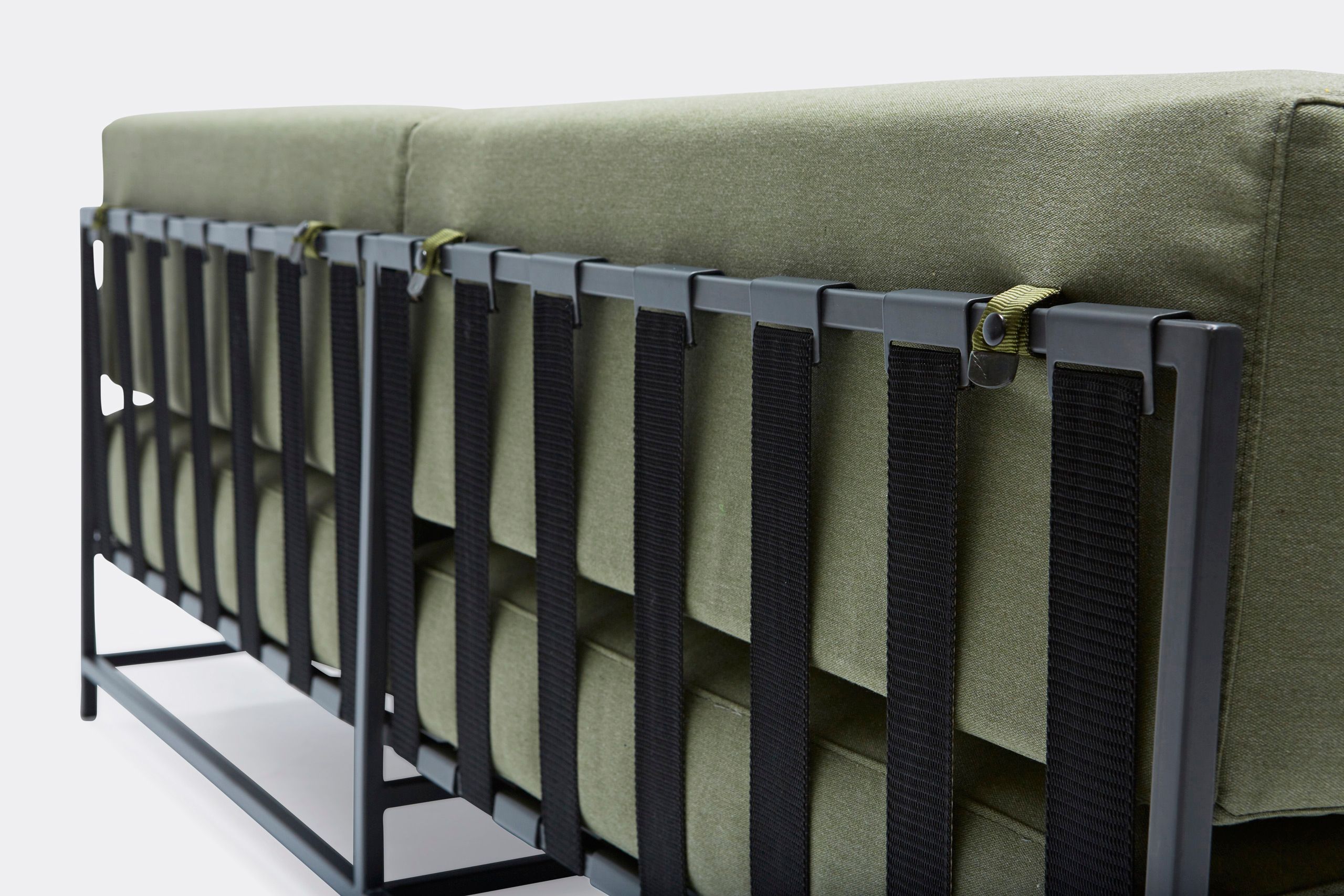 a steel framed sofa with black metal finish and green cushions and supporting belts on a white background .