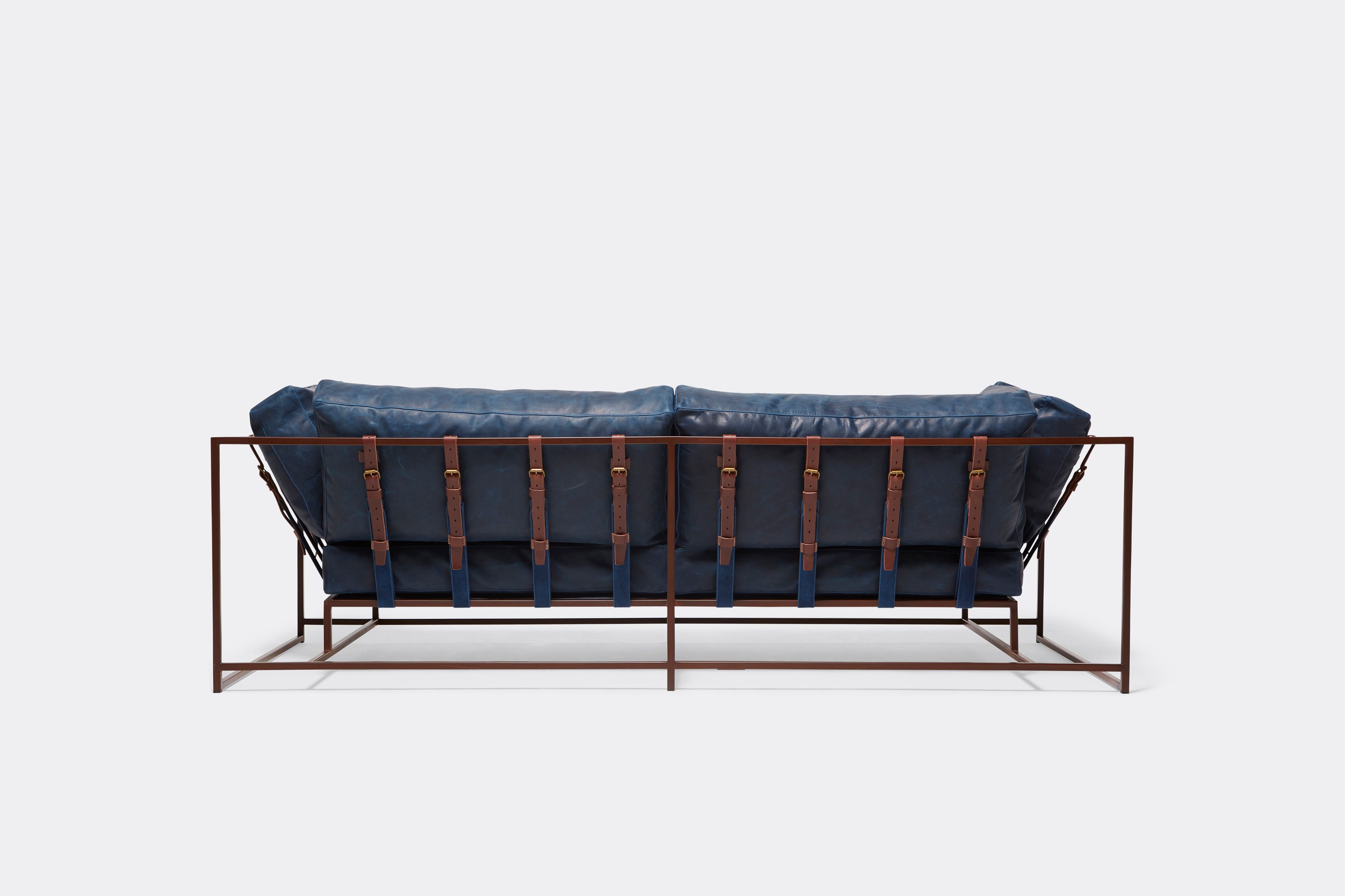 back of two seat sofa with blue leather upholstery and brown leather belts on marble rust metal frame