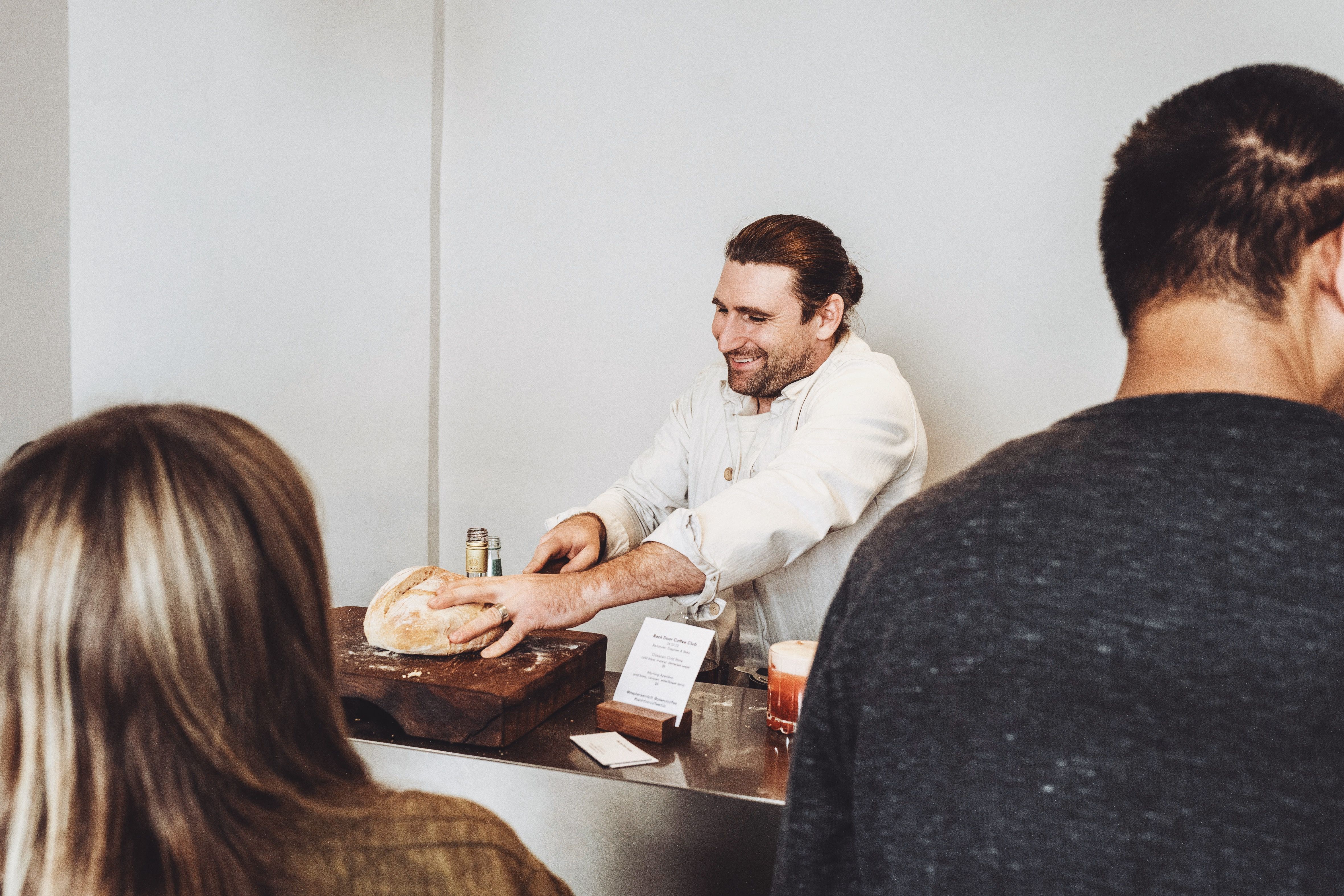 a man is cutting a loaf of bread in front of a group of people .