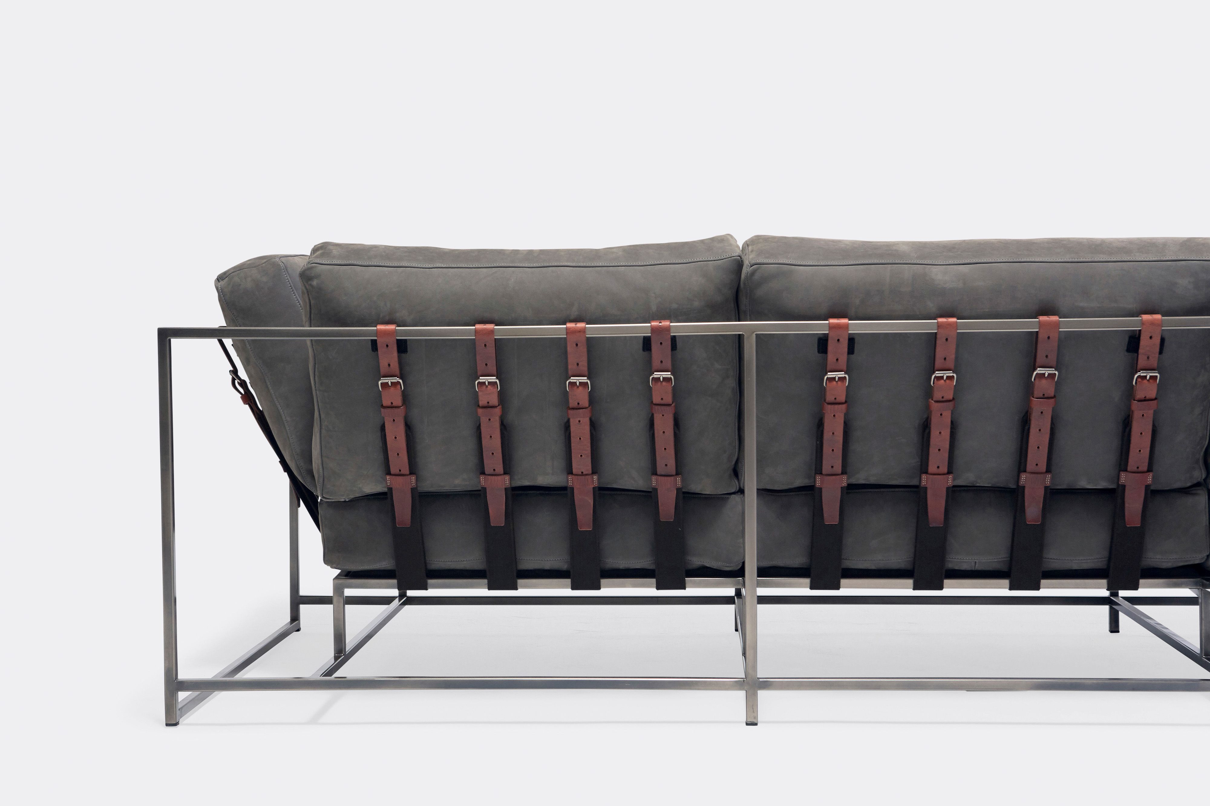 Back of sofa with grey leather upholstery and brown leather belts on antique nickel metal frame