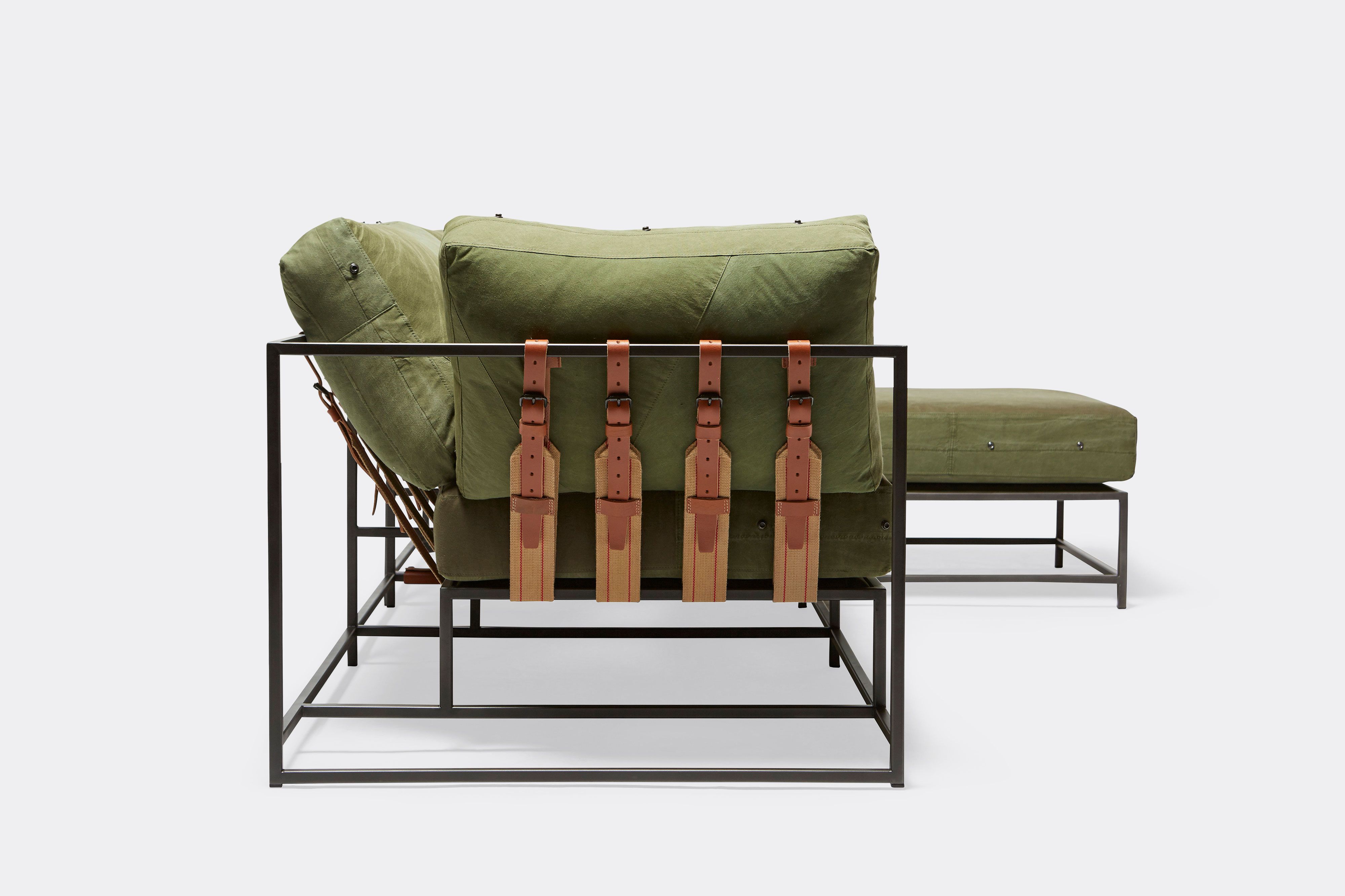 side of sectional with green canvas upholstery and brown leather belts on black metal frame