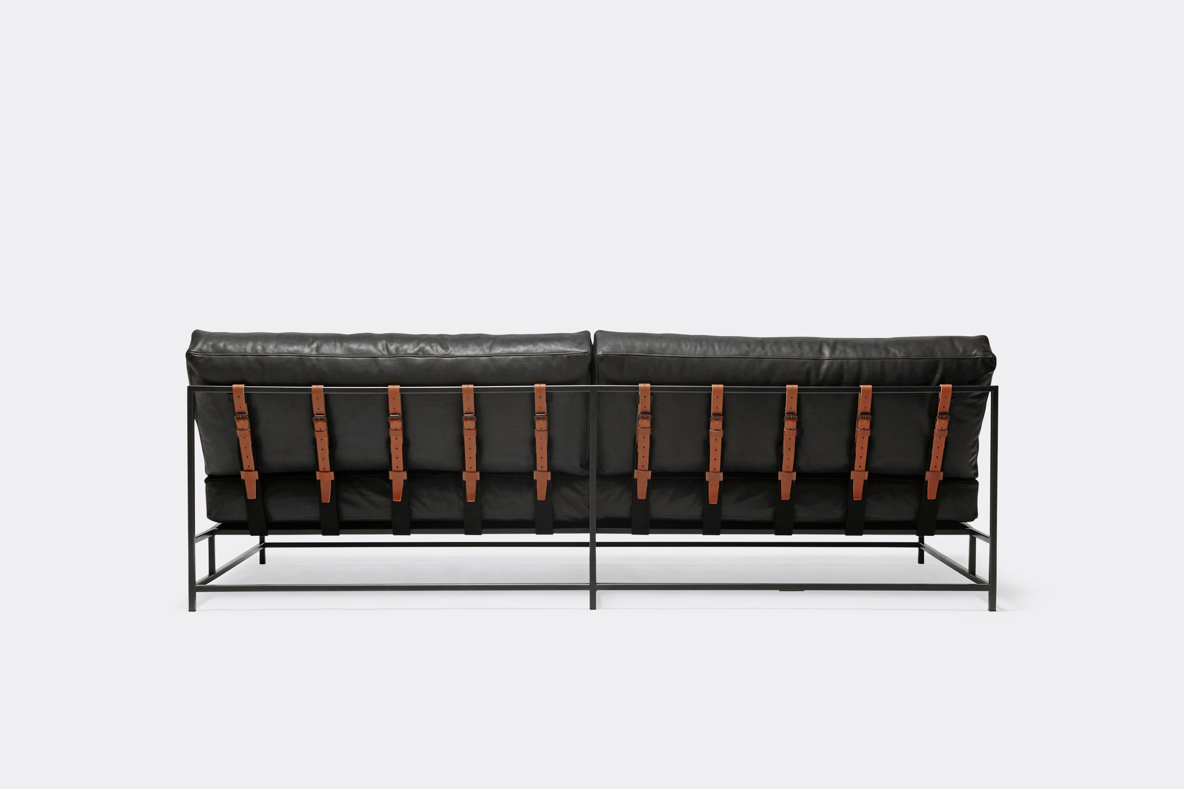 back of loveseat with black leather upholstery and brown leather belts on black metal frame