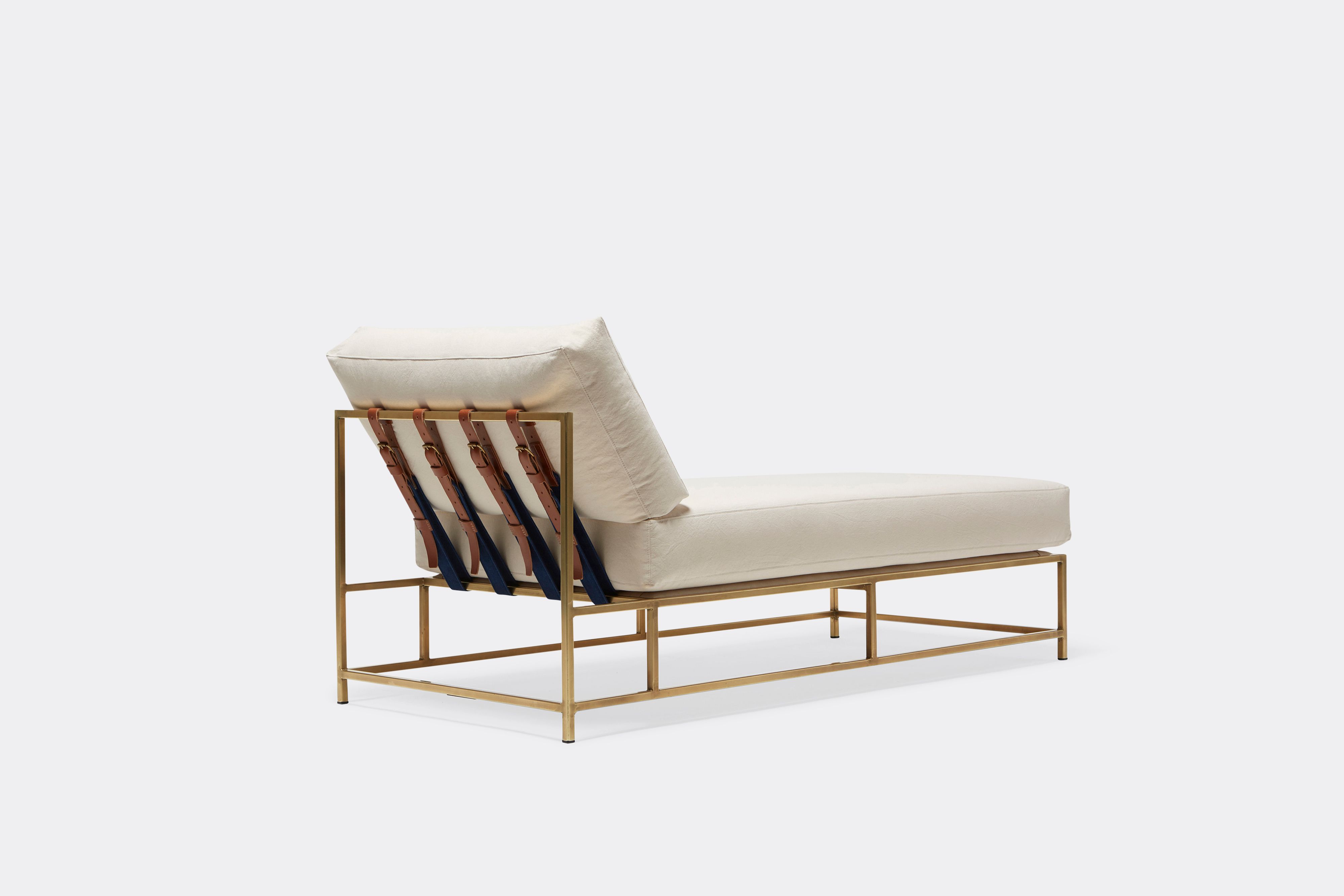 Sideview of lounge chaise with natural canvas upholstery and brown leather belt on tarnished brass metal frame