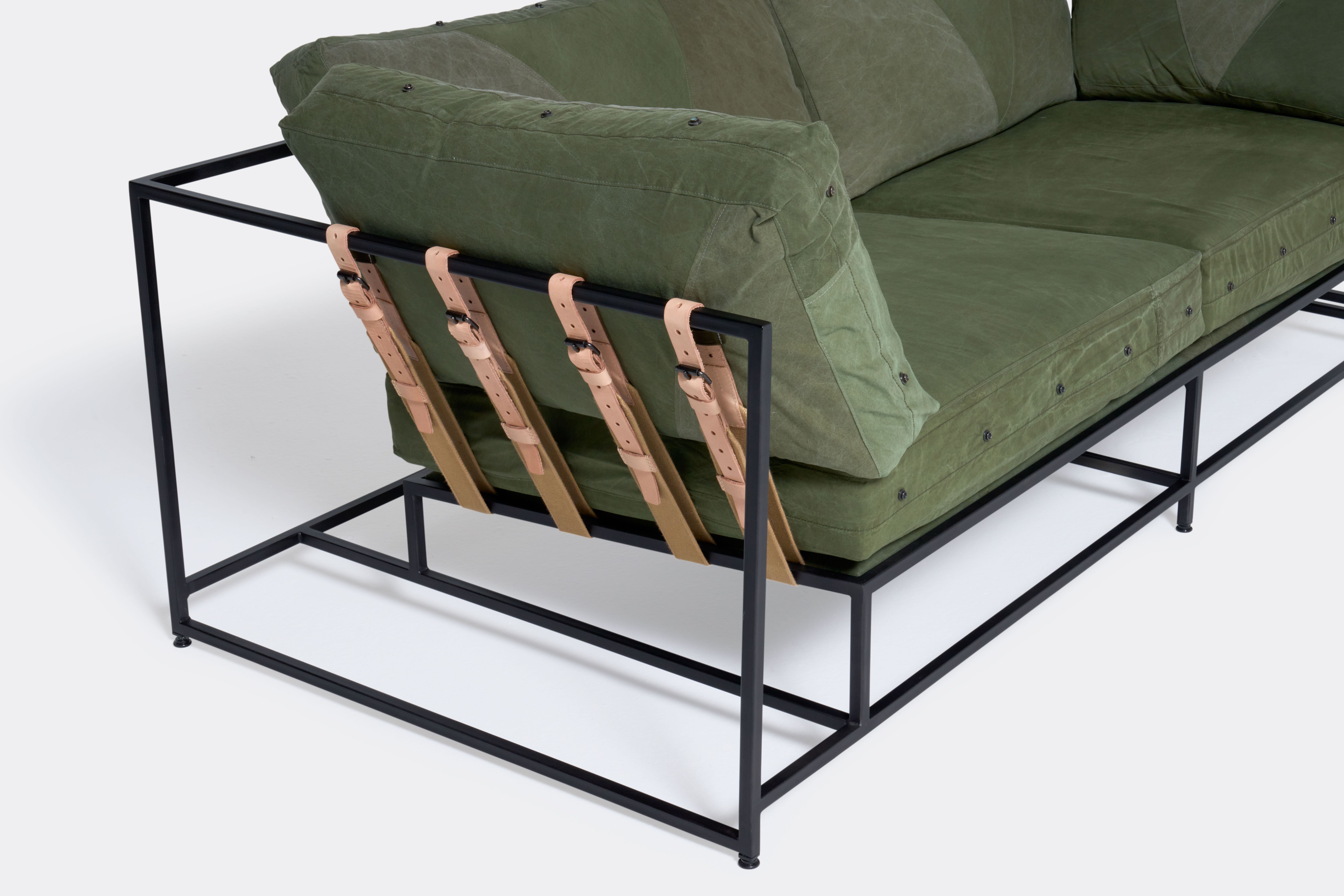 a green sofa with a black steel frame and green cushions on a white background .
