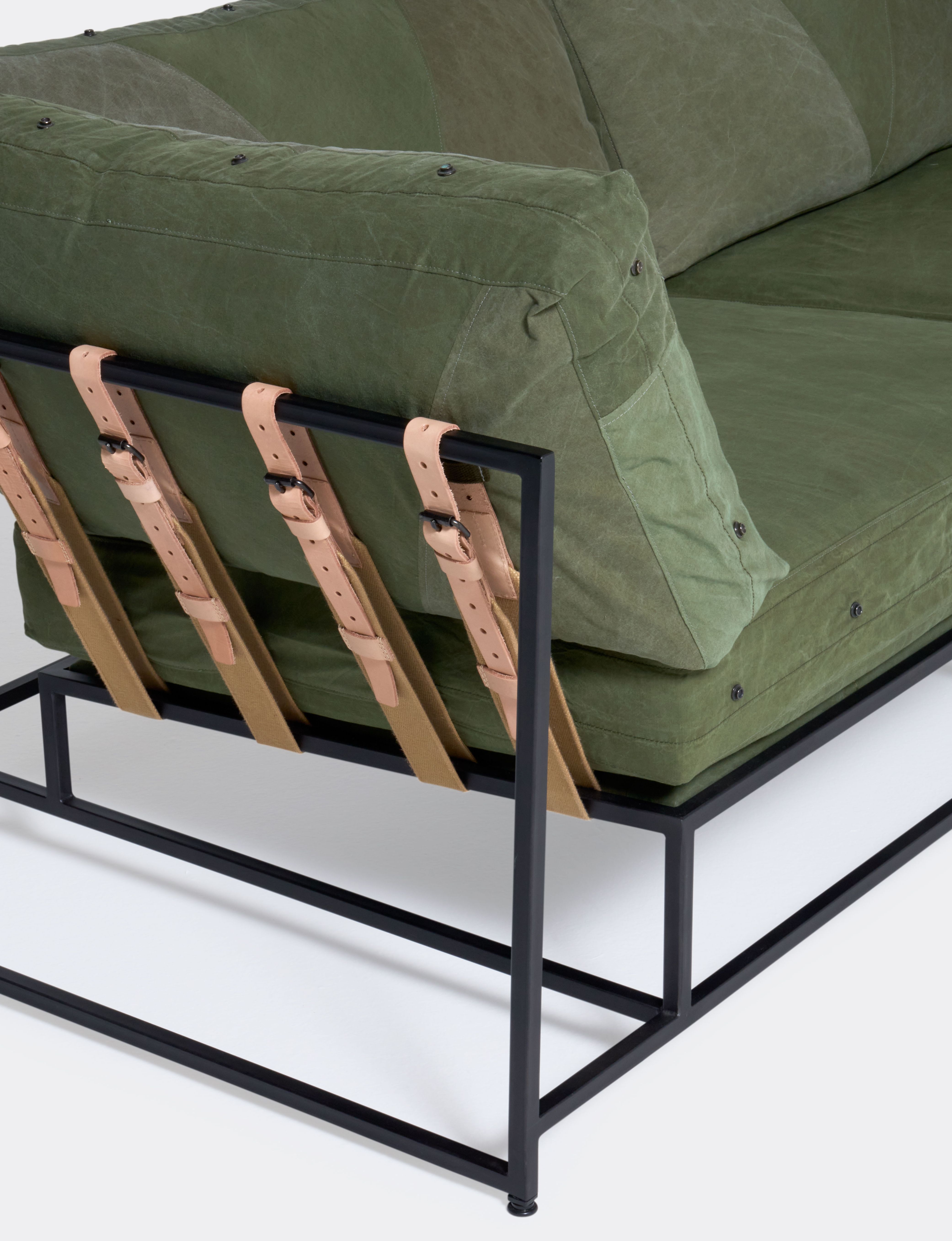 a green sofa with a black steel frame and green cushions on a white background .