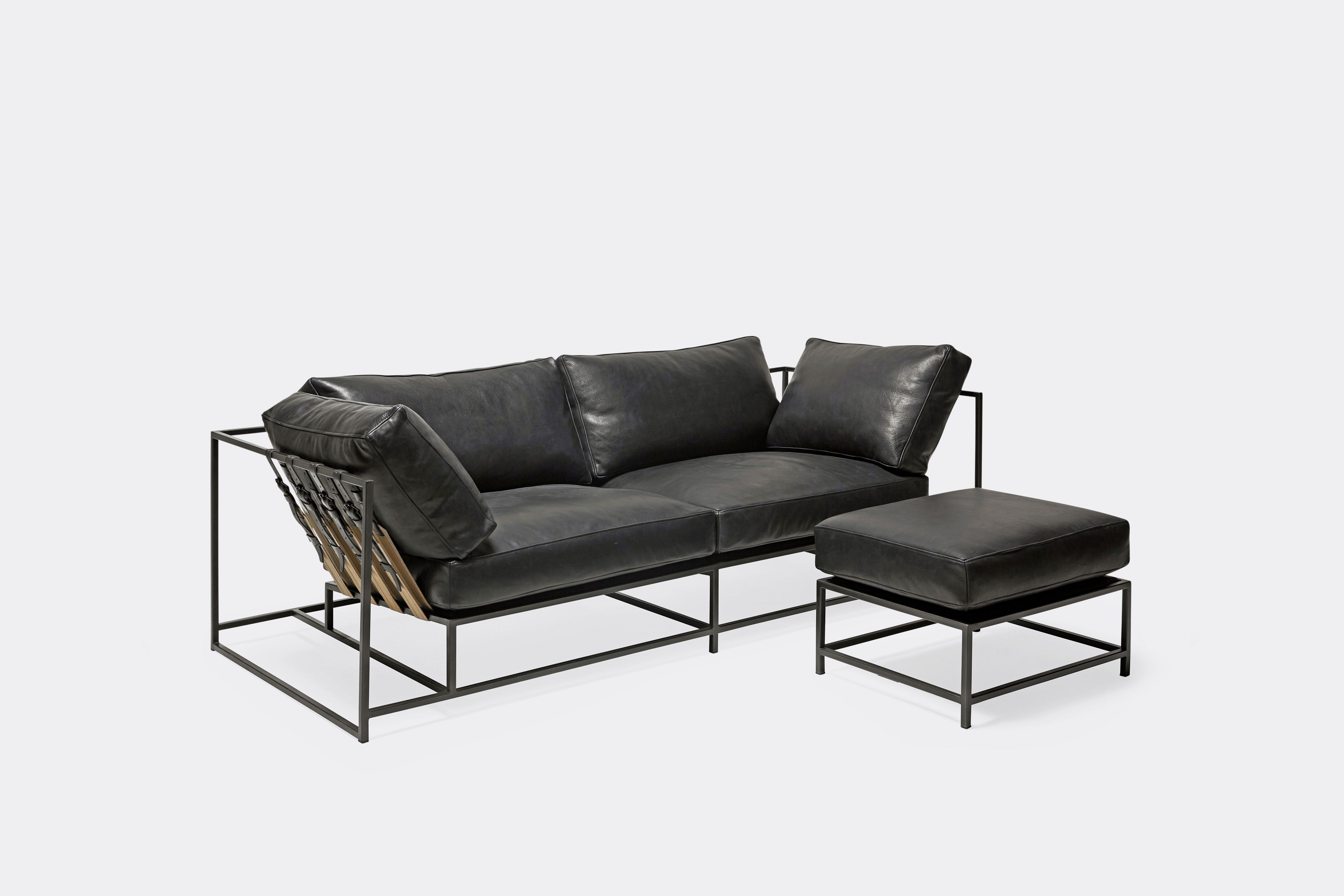 side of two seat sofa and ottoman black leather upholstery and black leather belts on black metal frame