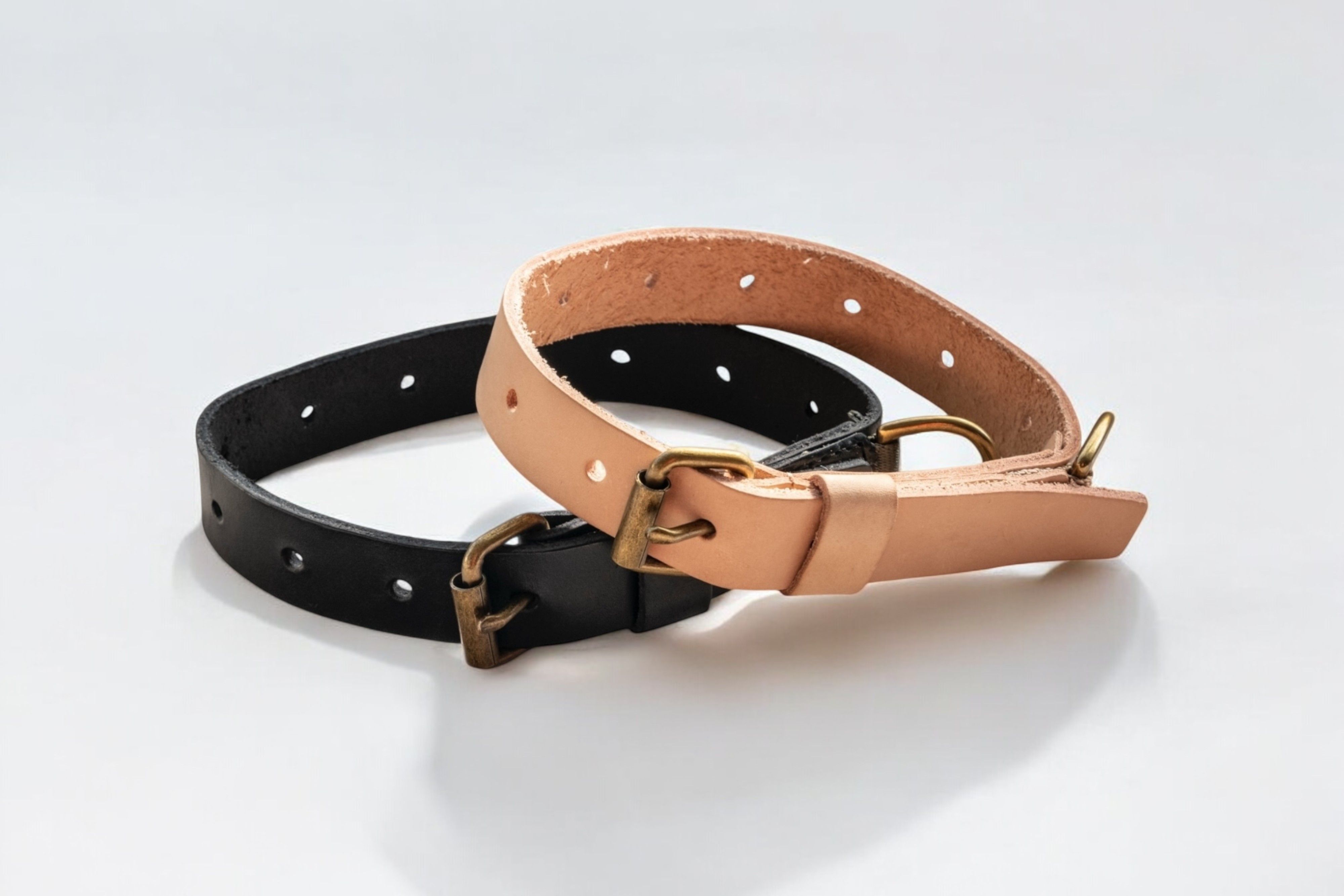 Two leather collars, one black and one natural tan, with brass buckles.