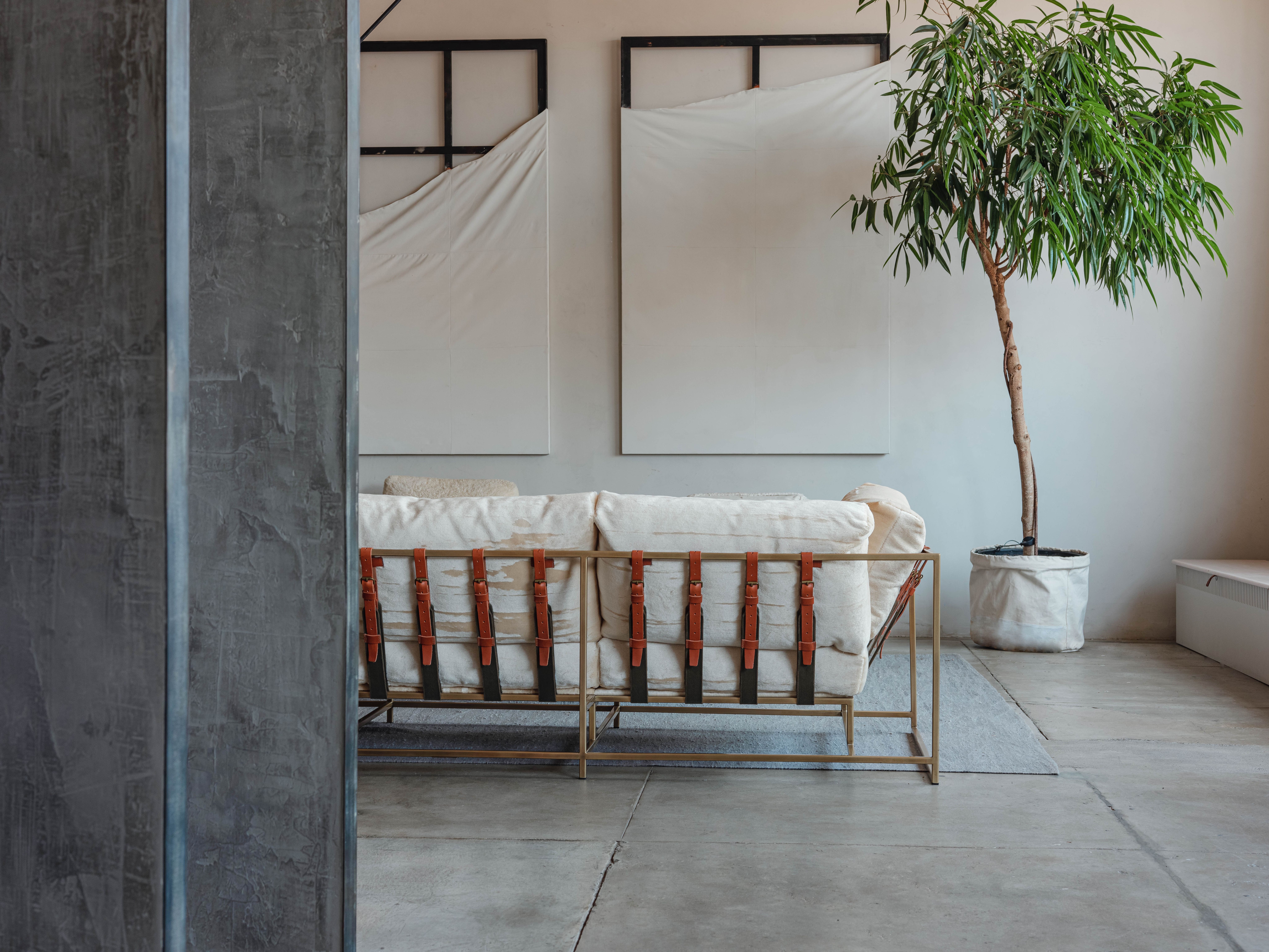 a living room with a Stephen Kenn Inheritance sofa in cream upholstery with brown leather belts is atop a concrete floor with a potted plant in the background .