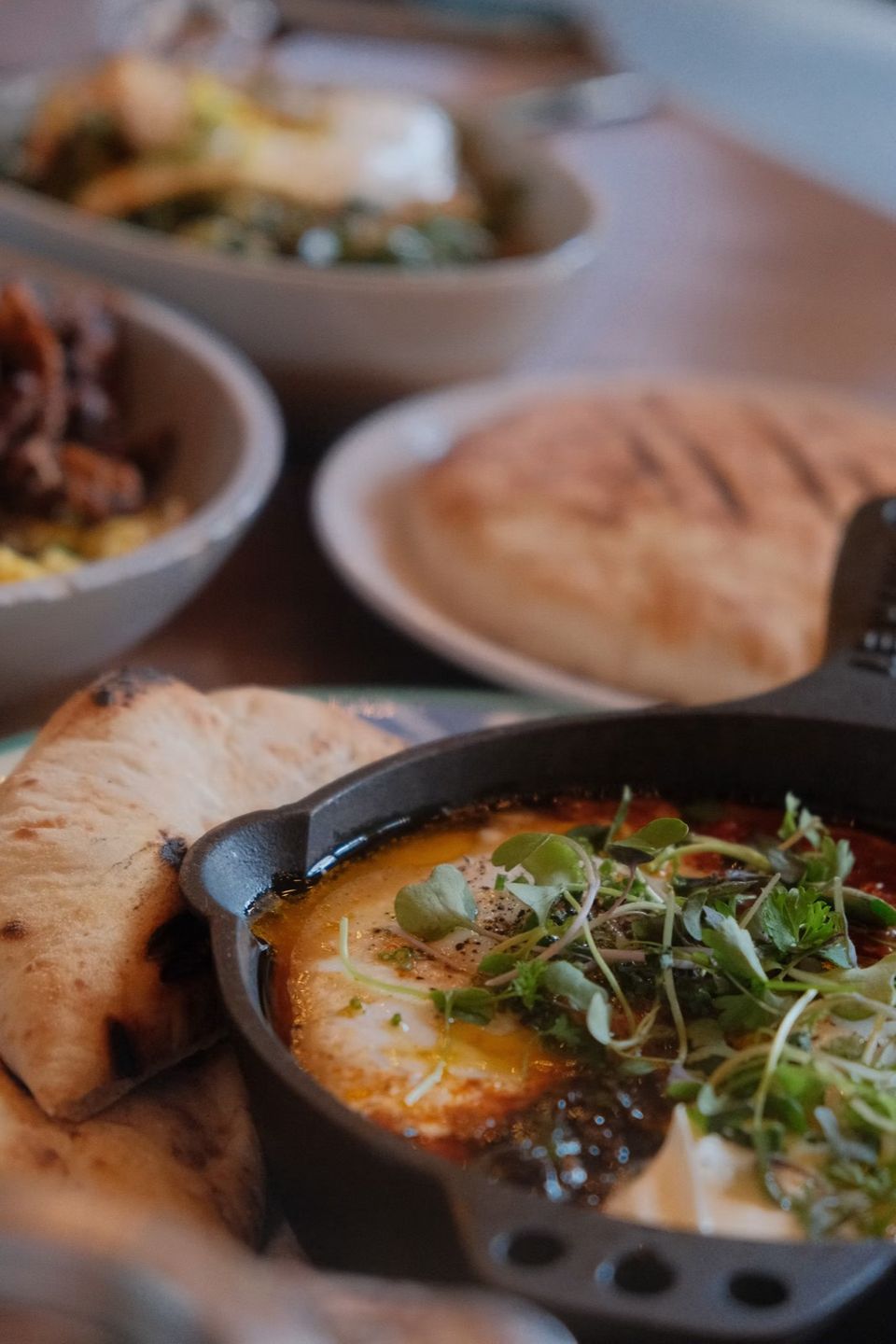 A shakshuka pan with herbs, flatbread and bowls of salad