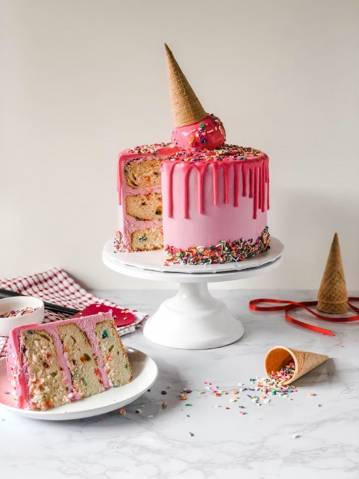 A pink drip cake with sprinkles and an ice-cream cone on top