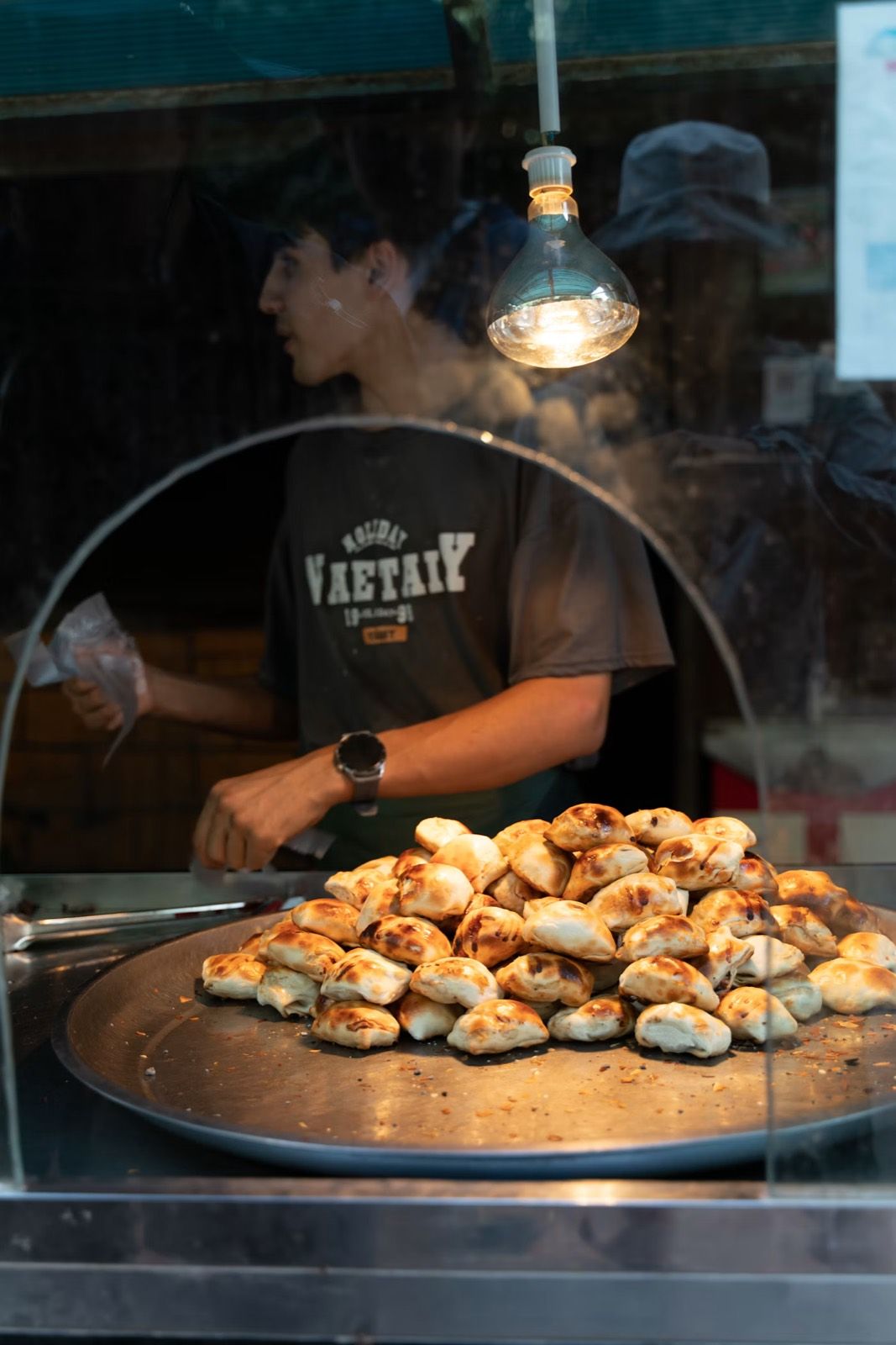 A stallholder serving a tray of golden pastries at a market